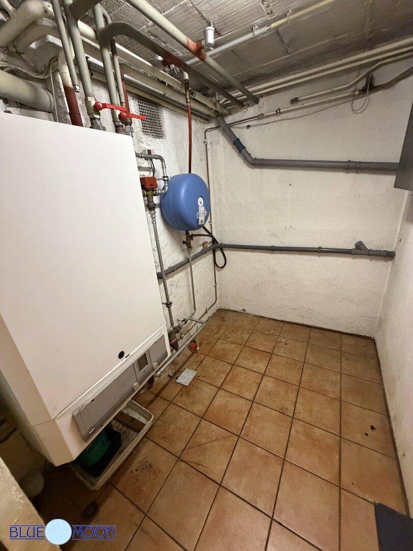 Heizungsraum im Keller mit Heizungsanlage, Rohren und Fliesenboden.