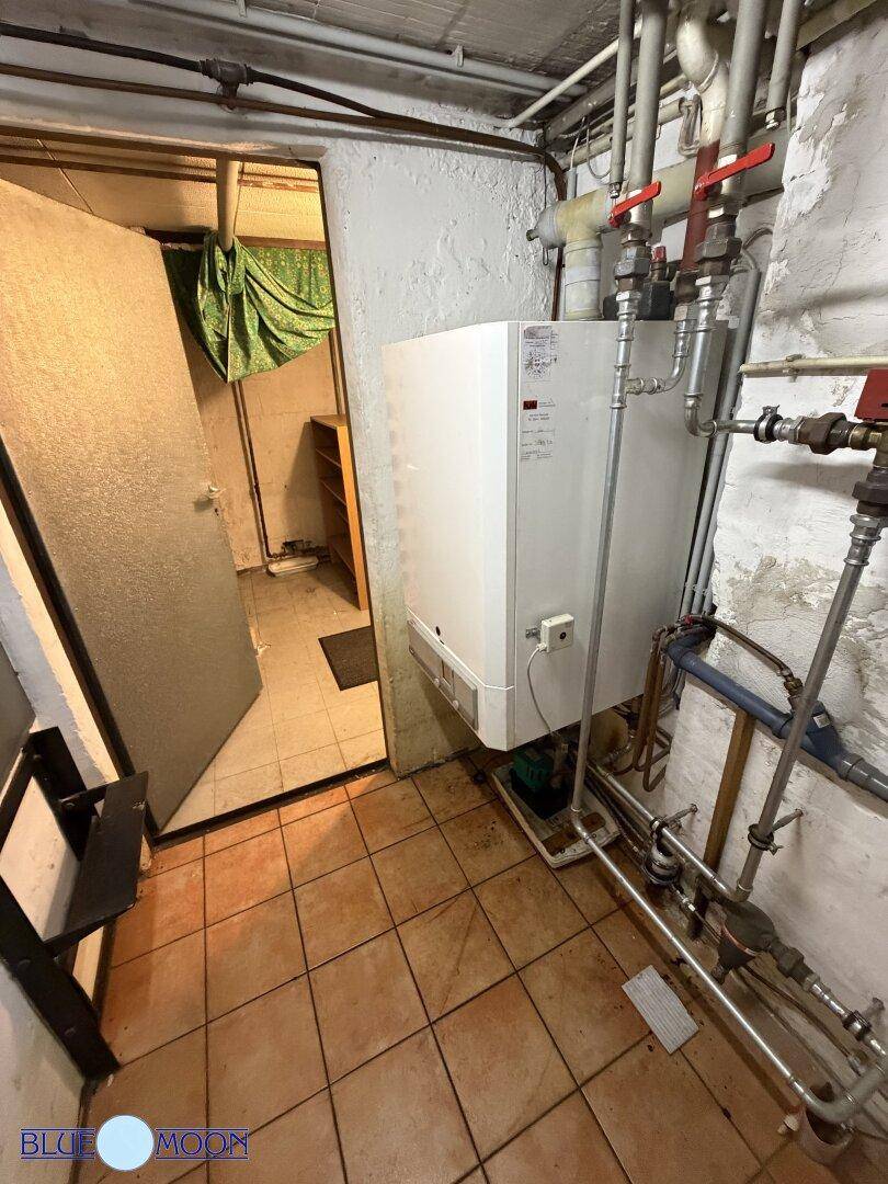 Kellerraum mit Heizungsanlage und sichtbaren Rohren, dient als Technikraum.