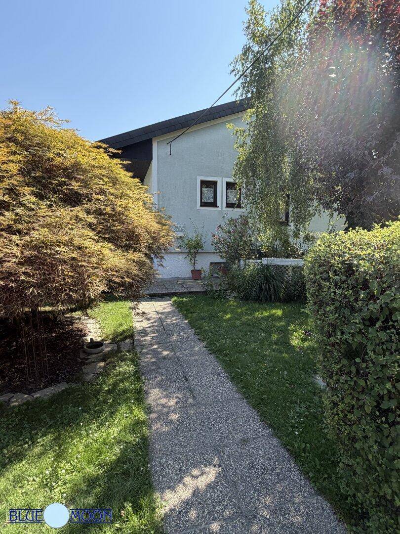 Vorderansicht des Hauses mit einem grünen Garten, einem gepflasterten Weg und üppiger Bepflanzung.