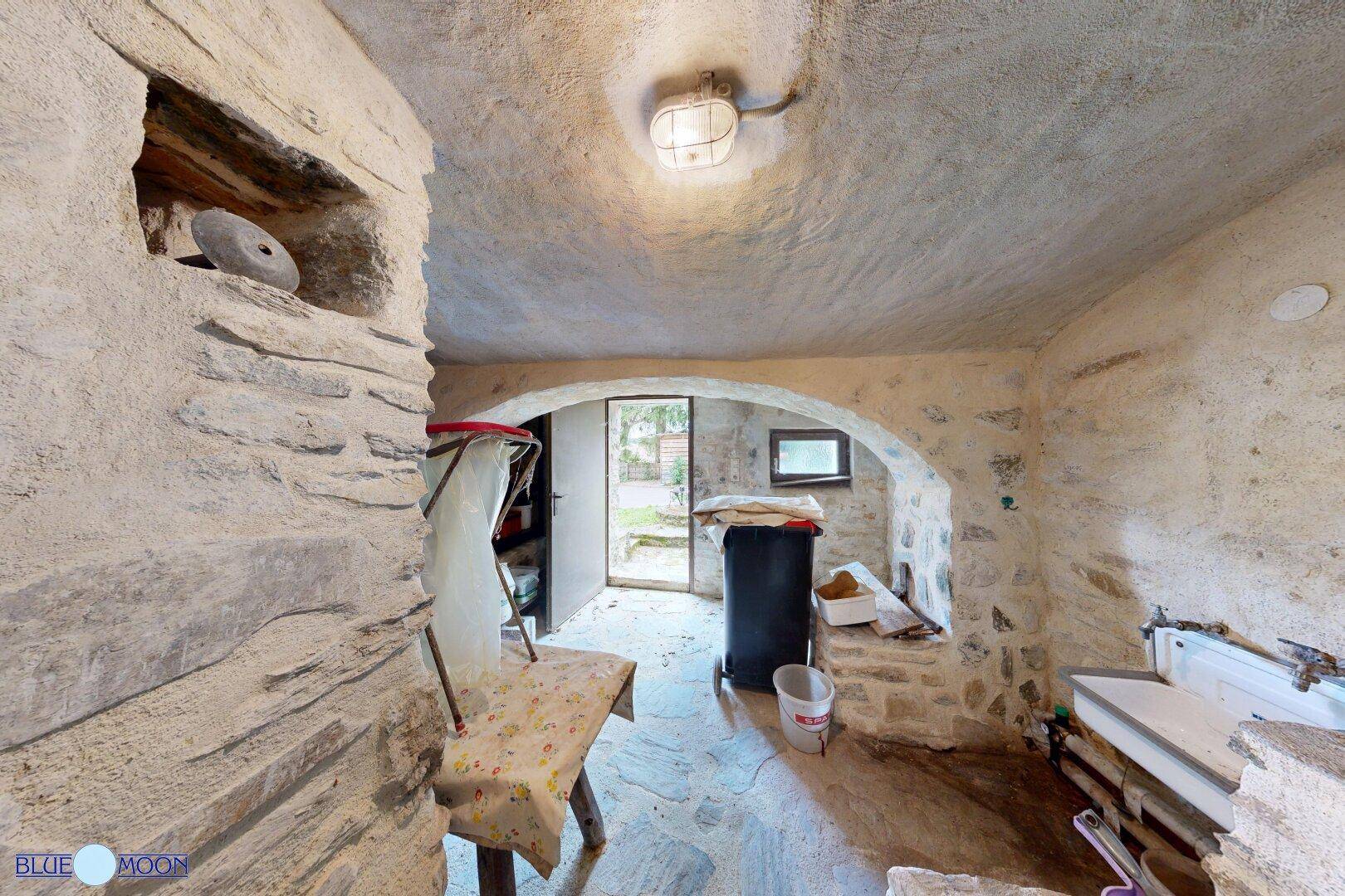 Kellerraum mit Natursteinwänden, einem Ausgang ins Freie und einem kleinen Fenster für Tageslicht.