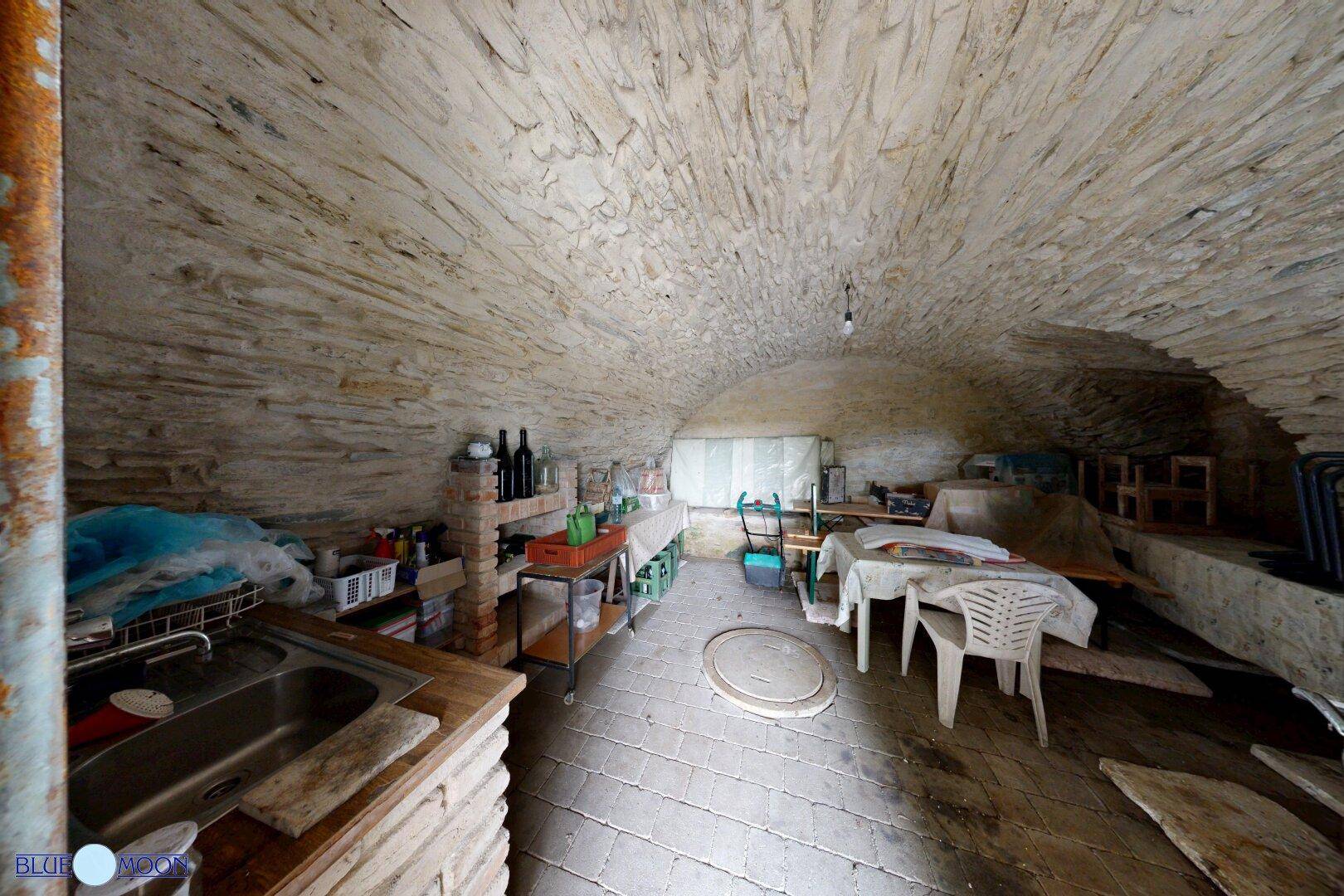 Gewölbekeller mit rustikalen Steinwänden und -decke, ausgestattet mit Spüle und Lagerflächen.