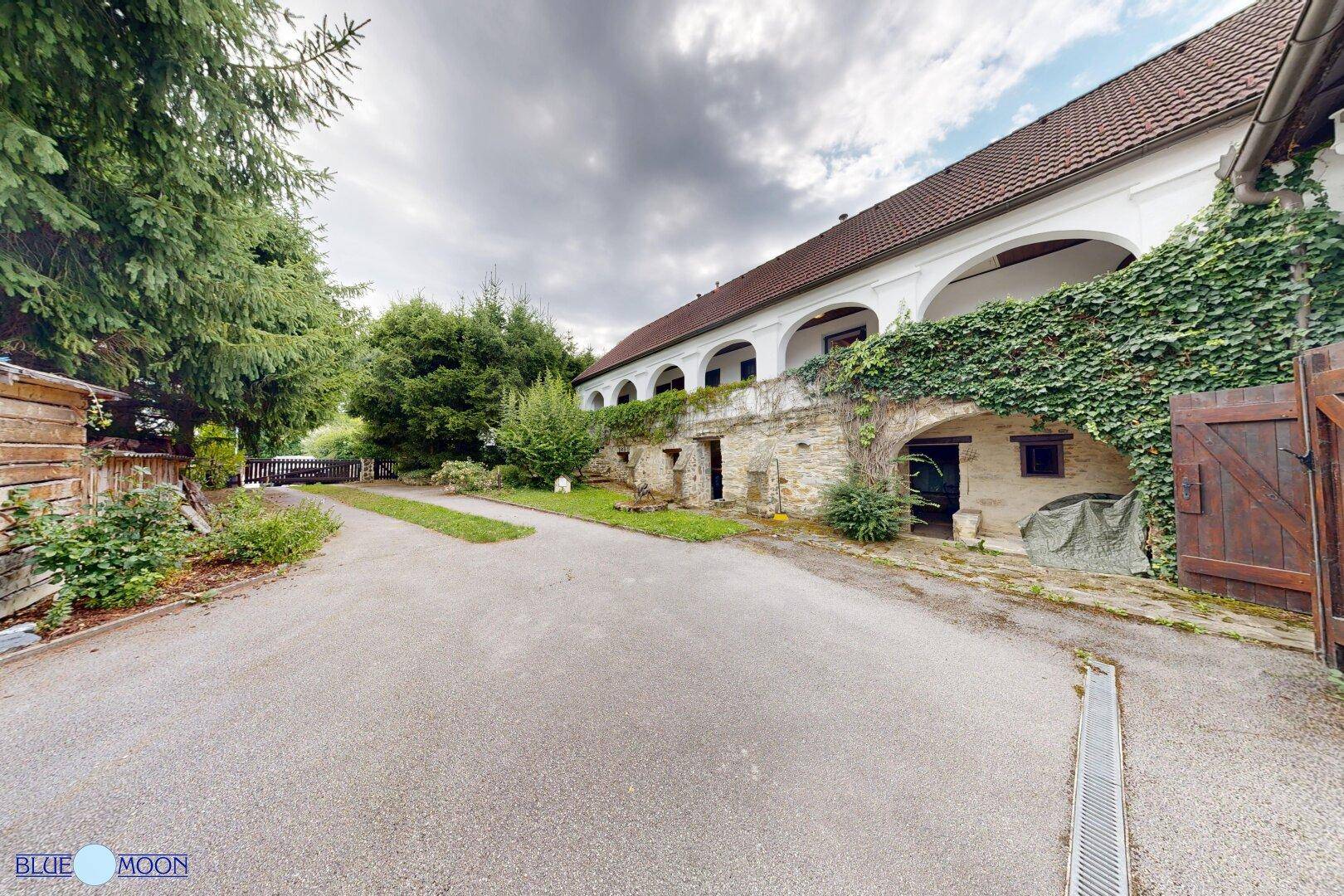 Historisches Anwesen mit bewachsenen Steinmauern und einem Nebengebäude unter bewölktem Himmel.