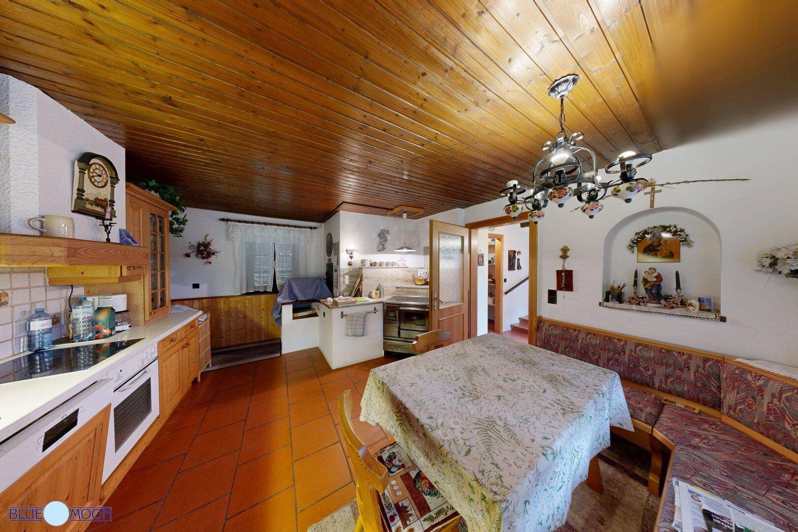 Rustikale Wohnküche mit Holzdecke, Terrakottafliesen und einem traditionellen Holzherd.