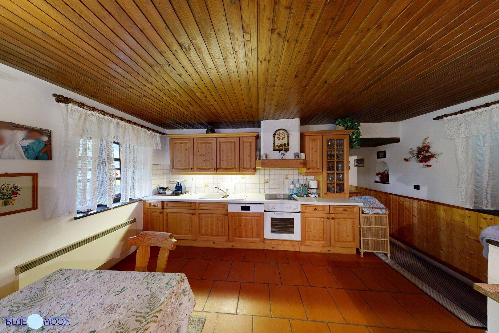Helle Wohnküche mit Holzschränken, Terrakottafliesen und einem Fenster mit Blick ins Grüne.