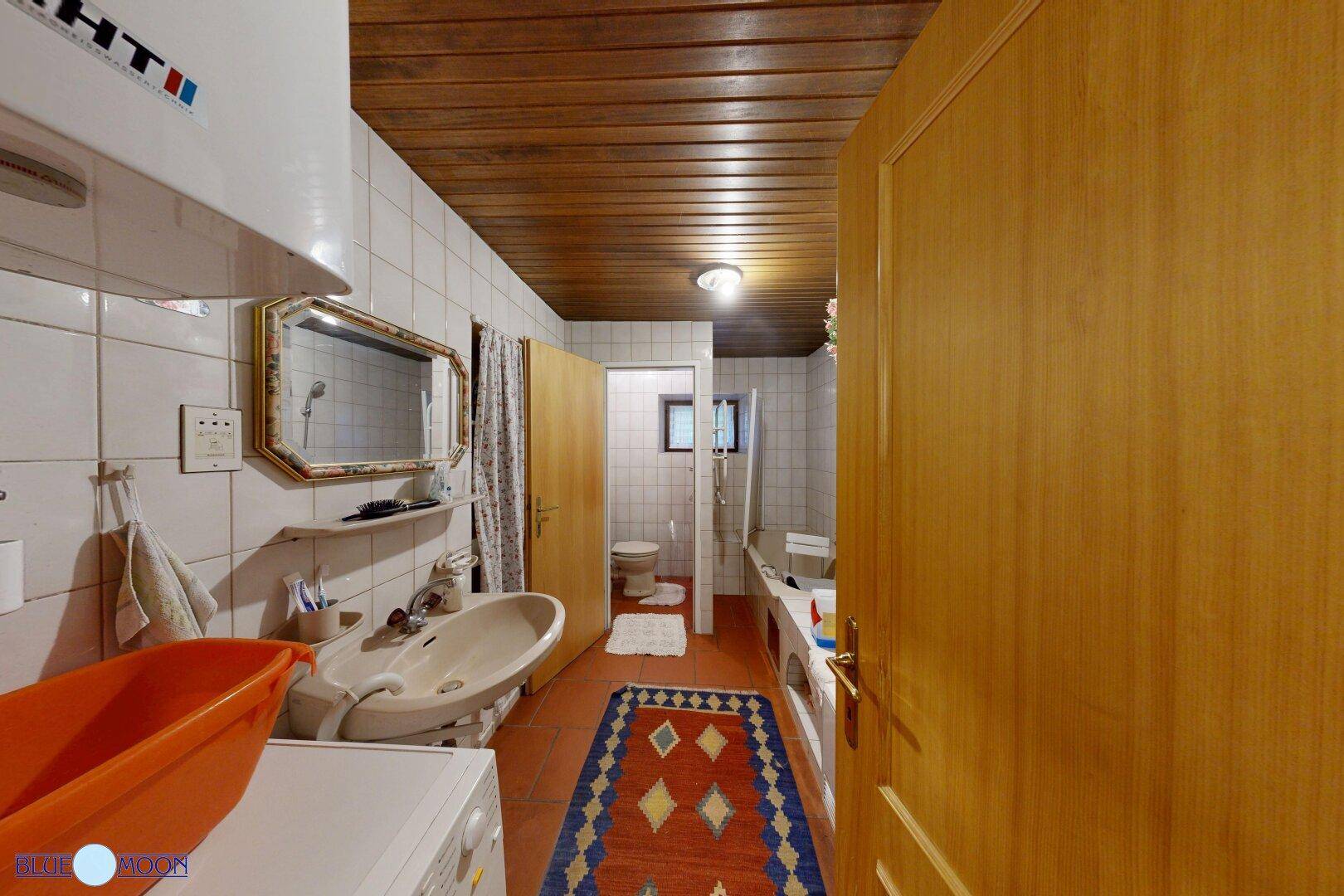 Funktionales Badezimmer mit weißen Fliesen, Holzdecke und Waschbecken, inklusive Waschmaschine.