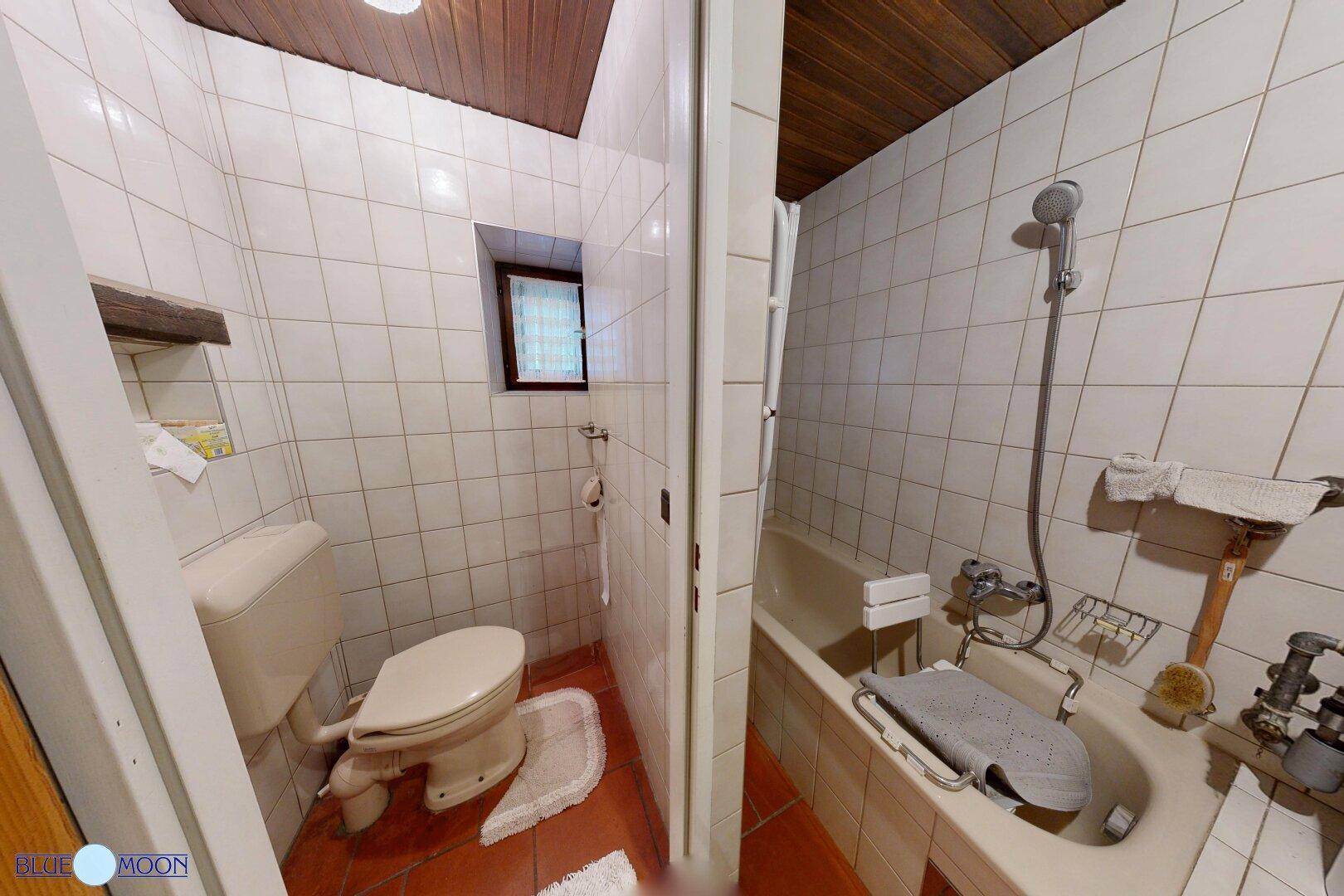 Kleines Badezimmer mit weißen Fliesen, Toilette und Badewanne mit Duschfunktion.