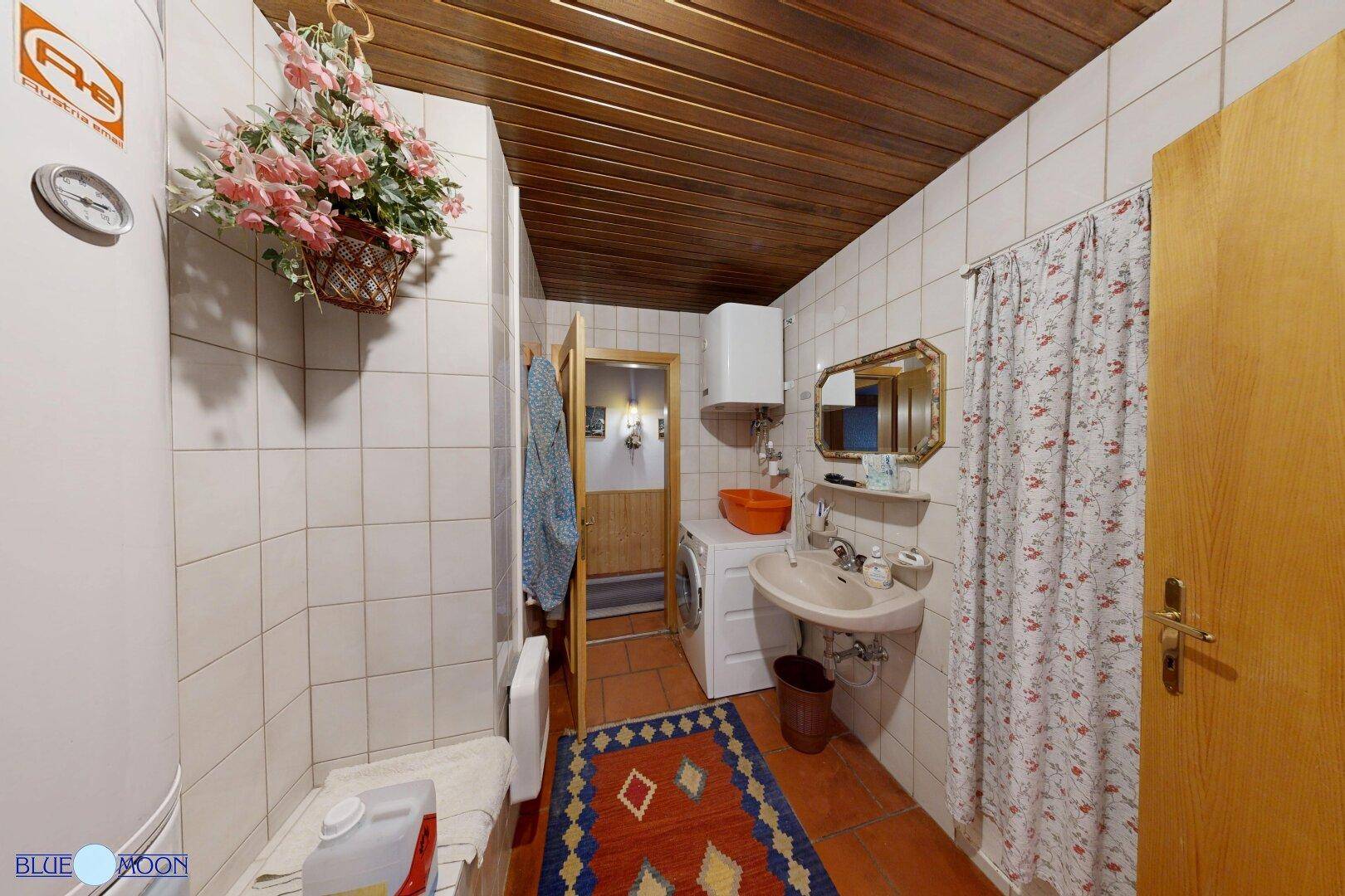 Praktisches Badezimmer mit weißen Fliesen, Holzdecke und Waschmaschine, gut beleuchtet.
