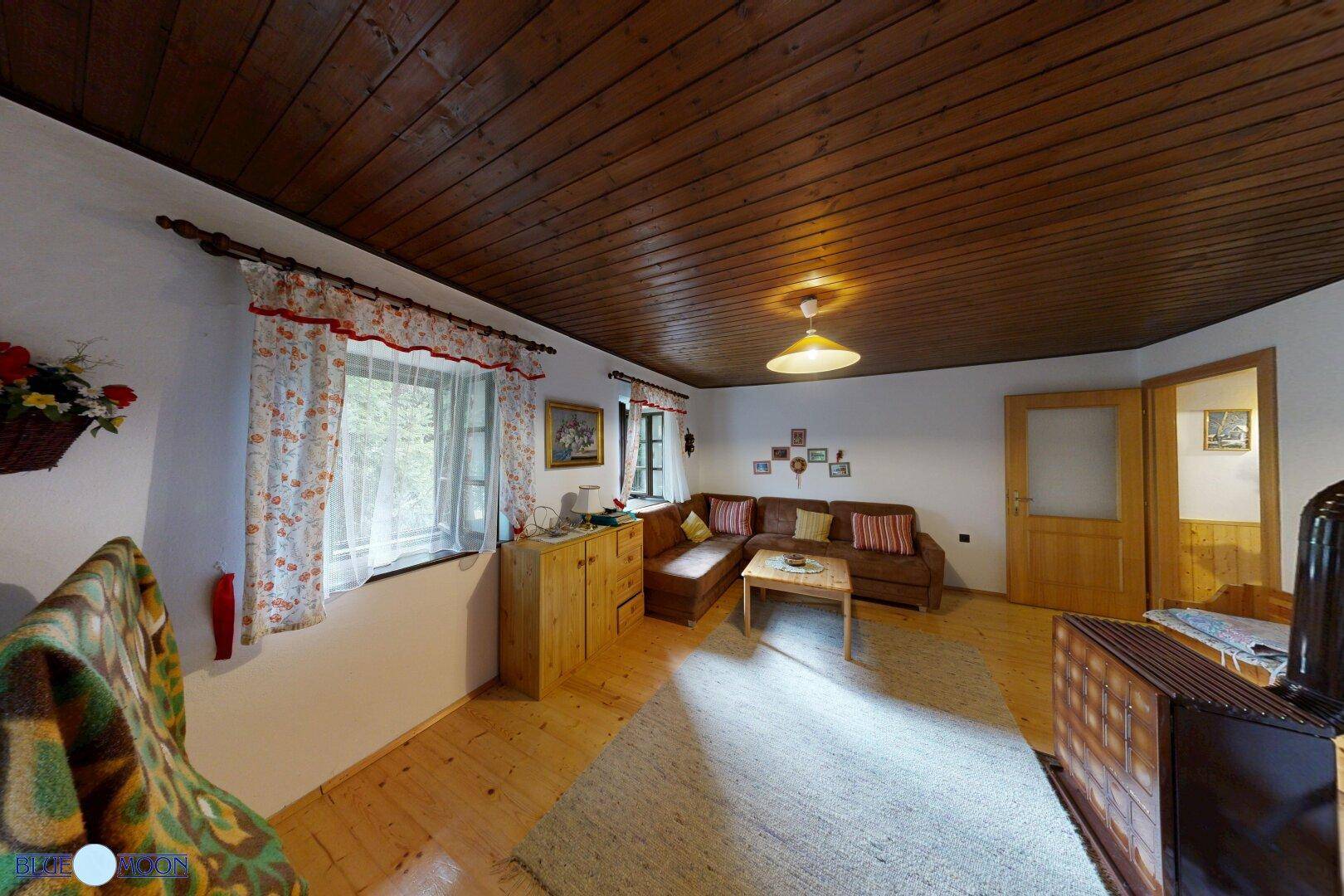 Gemütliches Wohnzimmer im Landhausstil mit Holzbalkendecke, Kaminofen und traditionellen Möbeln.