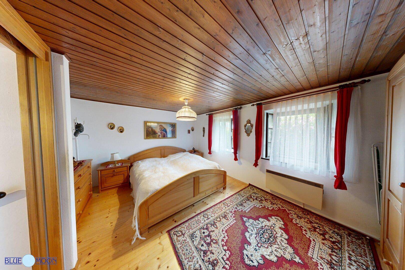 Schlafzimmer im Landhausstil mit Holzboden, Holzbalkendecke und einem großen Doppelbett.