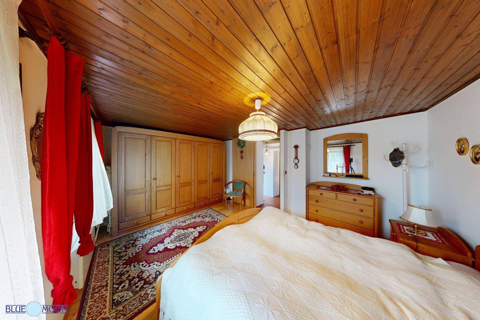 Schlafzimmer mit Holzboden, Holzbalkendecke und traditionellen Möbeln, inklusive Kommode und Spiegel.