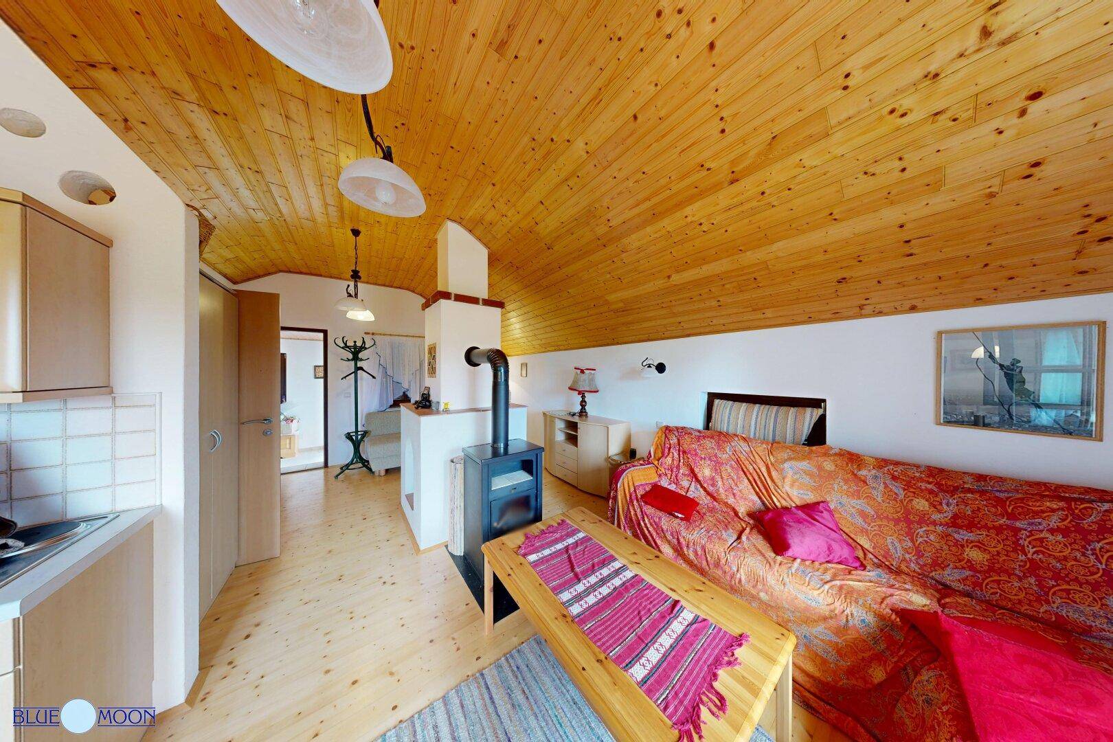 Wohnbereich im Dachgeschoss mit Kaminofen, Holzbalkendecke und gemütlicher Sitzecke.