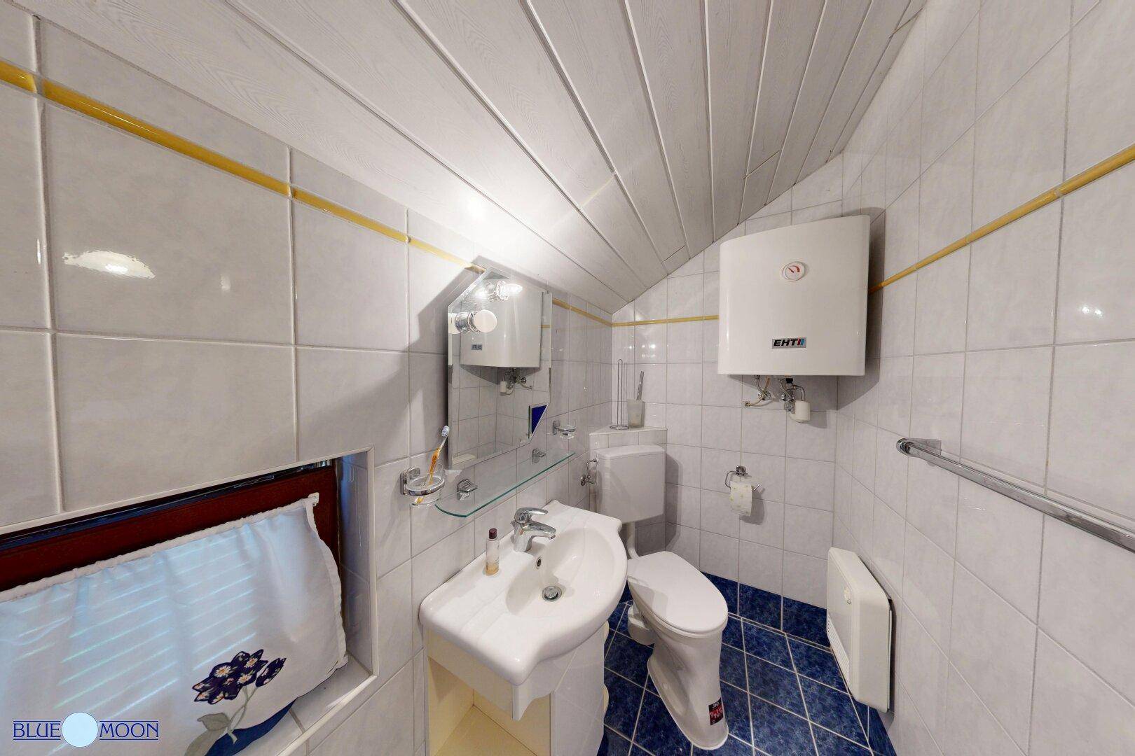 Kleines Badezimmer im Dachgeschoss mit blauen Fliesen, Waschbecken und Toilette.