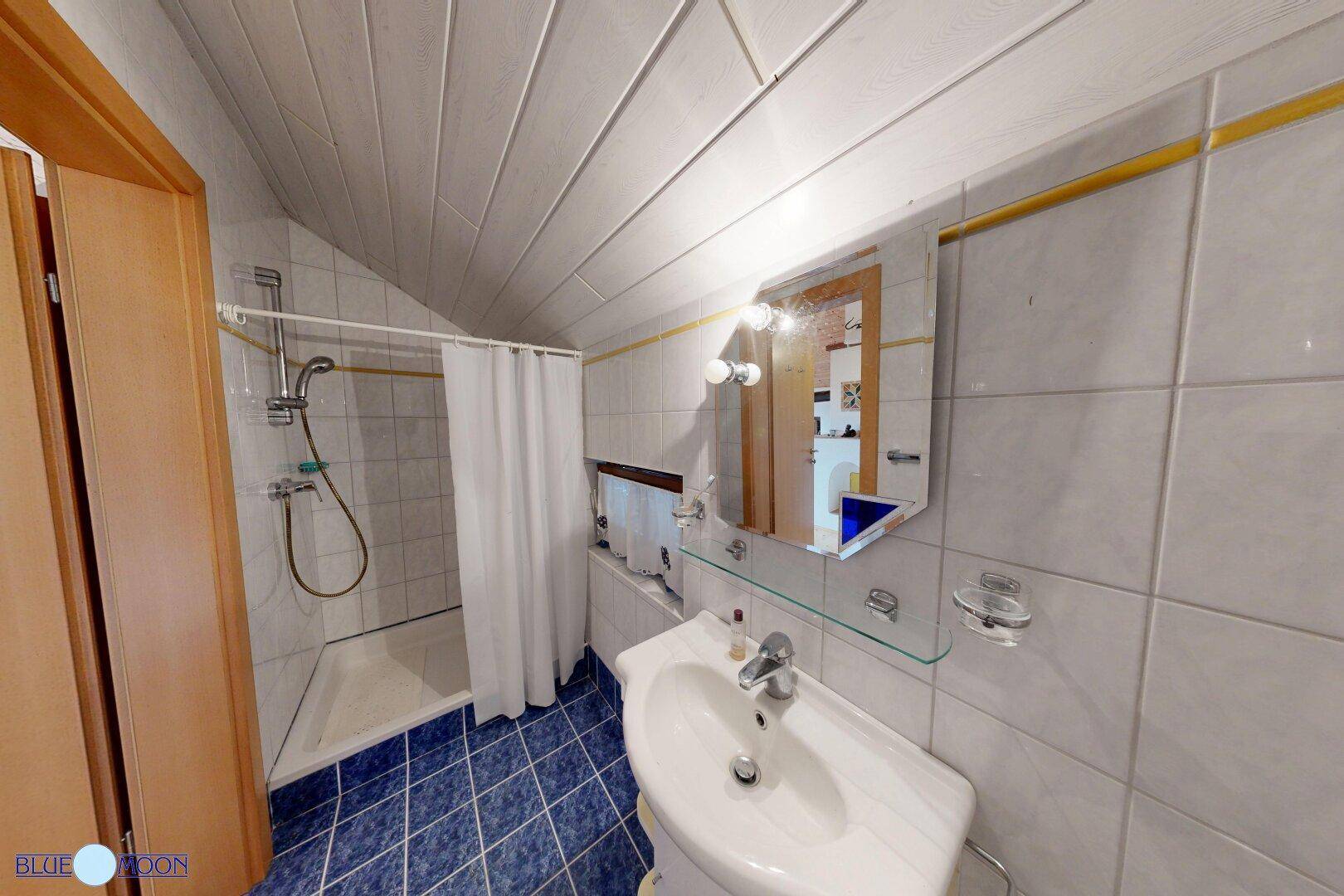 Badezimmer im Dachgeschoss mit Dusche, Waschbecken und Spiegel, in traditionellem Stil.
