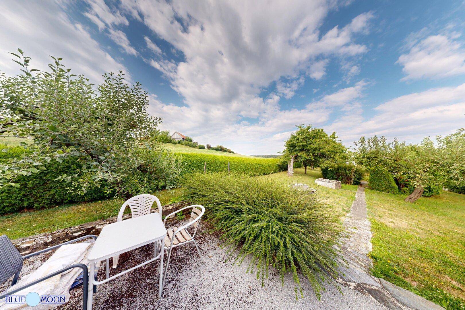 Gemütliche Sitzecke im Garten mit Tisch und Stühlen, umgeben von viel Grün.