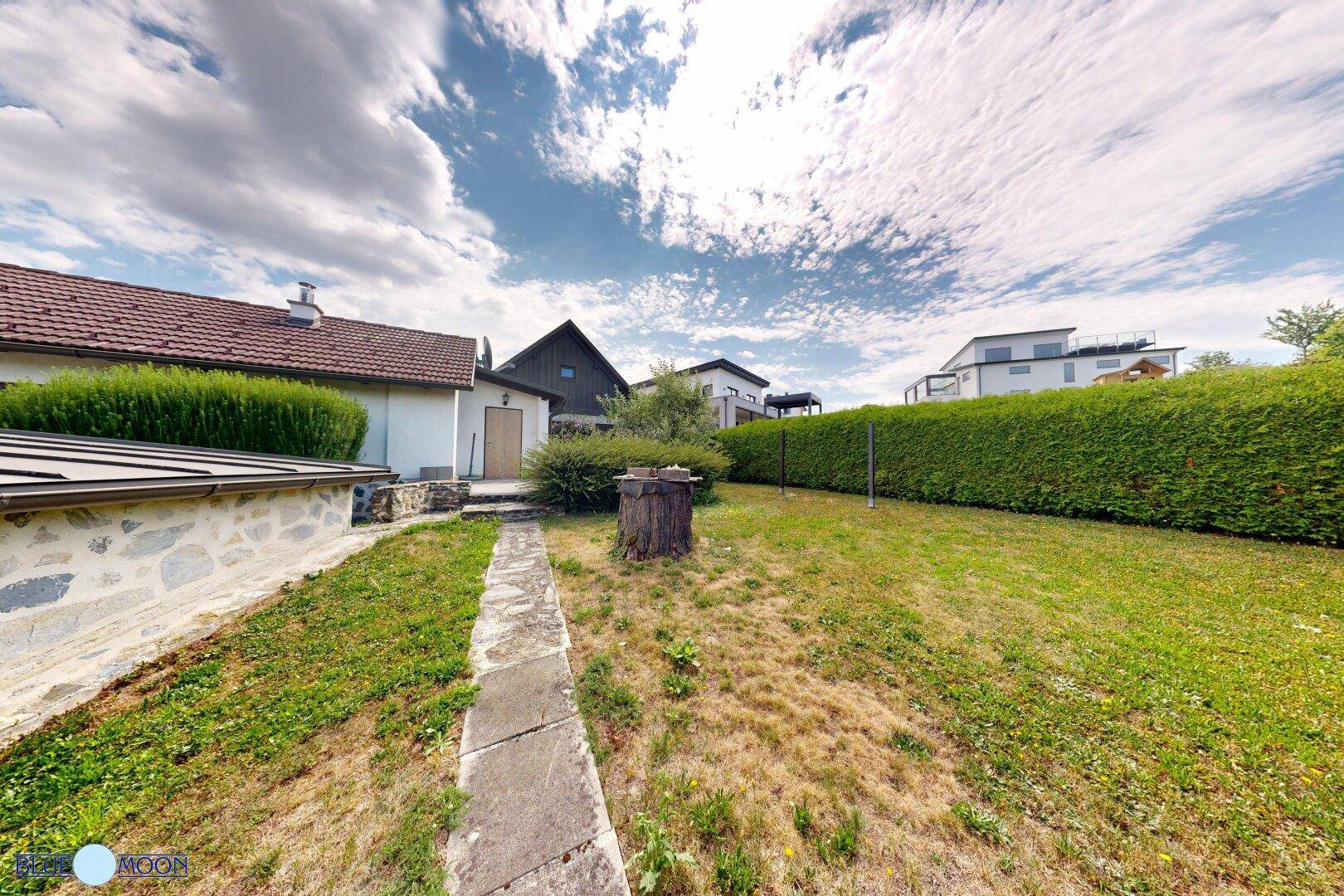 Gepflegter Garten mit Rasenfläche, Hecken und einem Weg, der zum Haus führt.