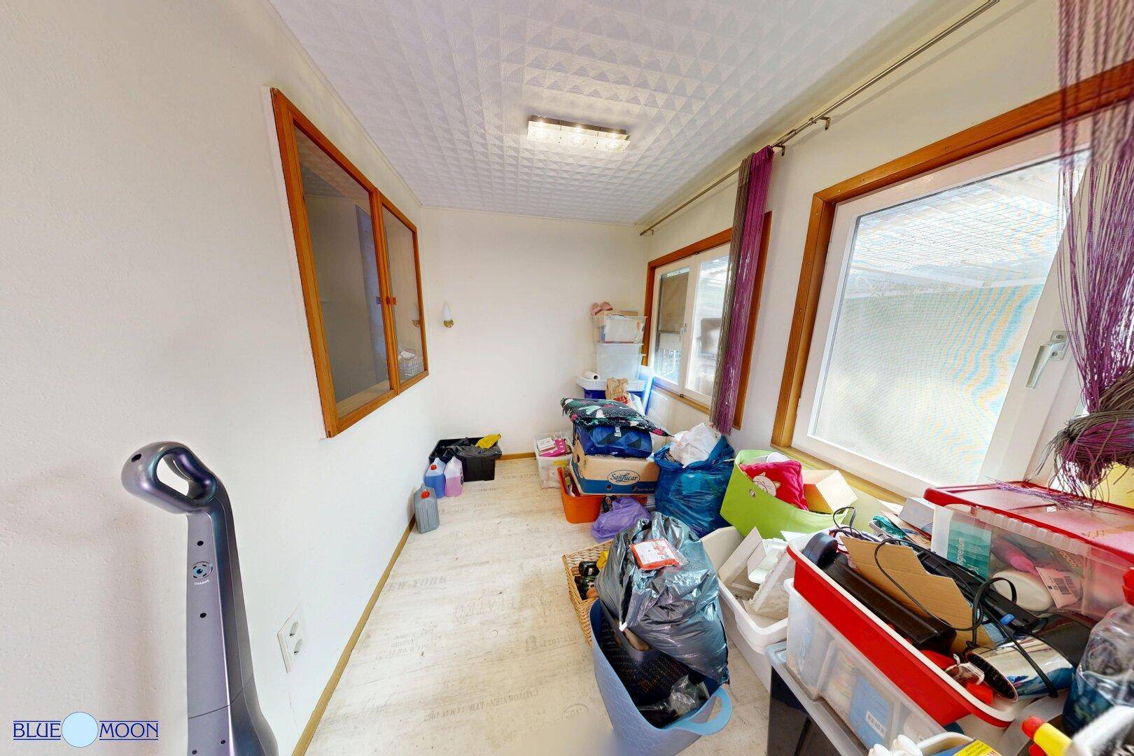 Abstellraum mit vielen Kisten und Gegenständen, hell durch große Fenster.