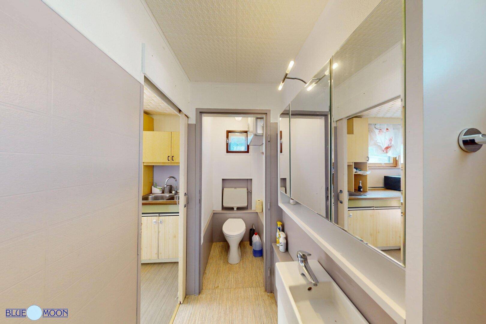Kleines Badezimmer mit WC, Waschbecken und Spiegel, angrenzend an die Küche.