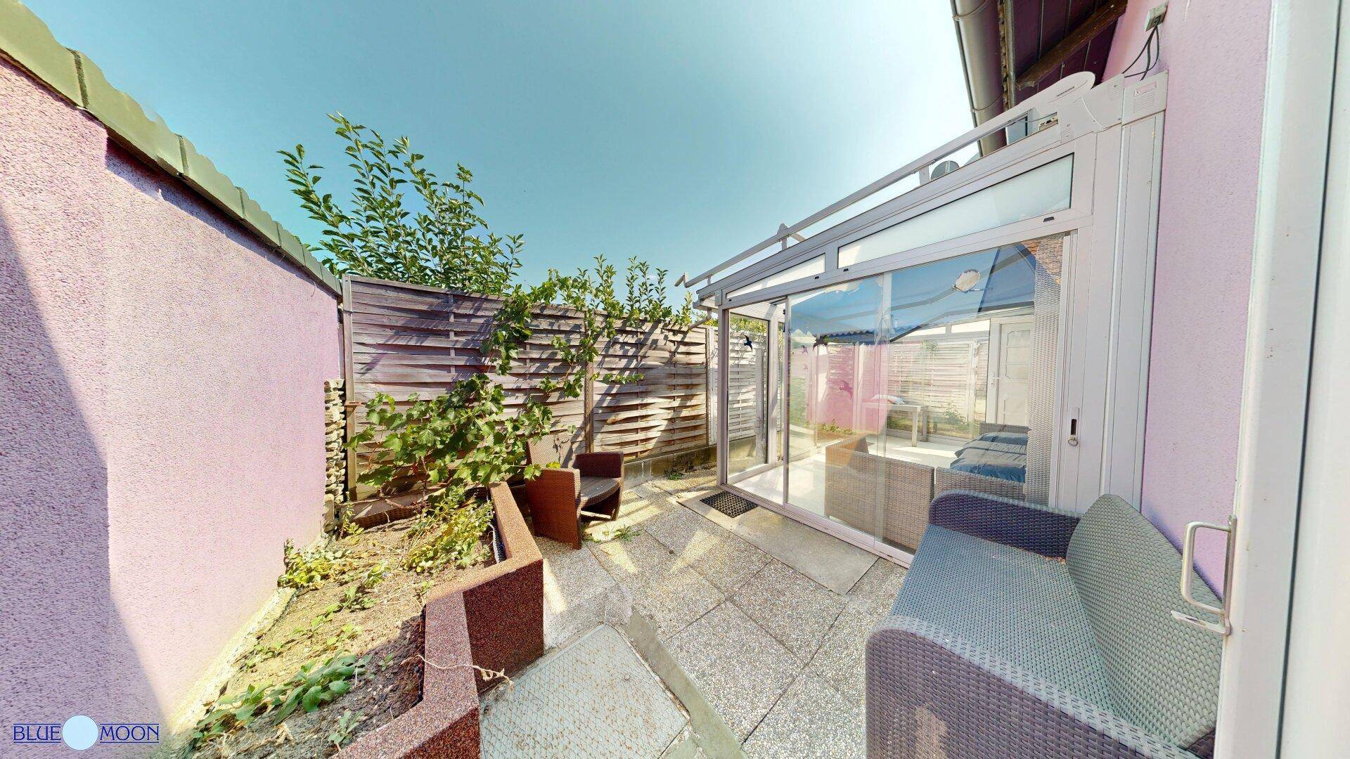 Terrasse mit Zugang zum Wintergarten, umgeben von einer Holzwand und Pflanzen.