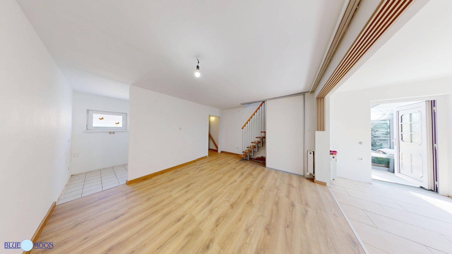 Geräumiger Wohnbereich mit Laminatboden und offener Holztreppe zum Obergeschoss.