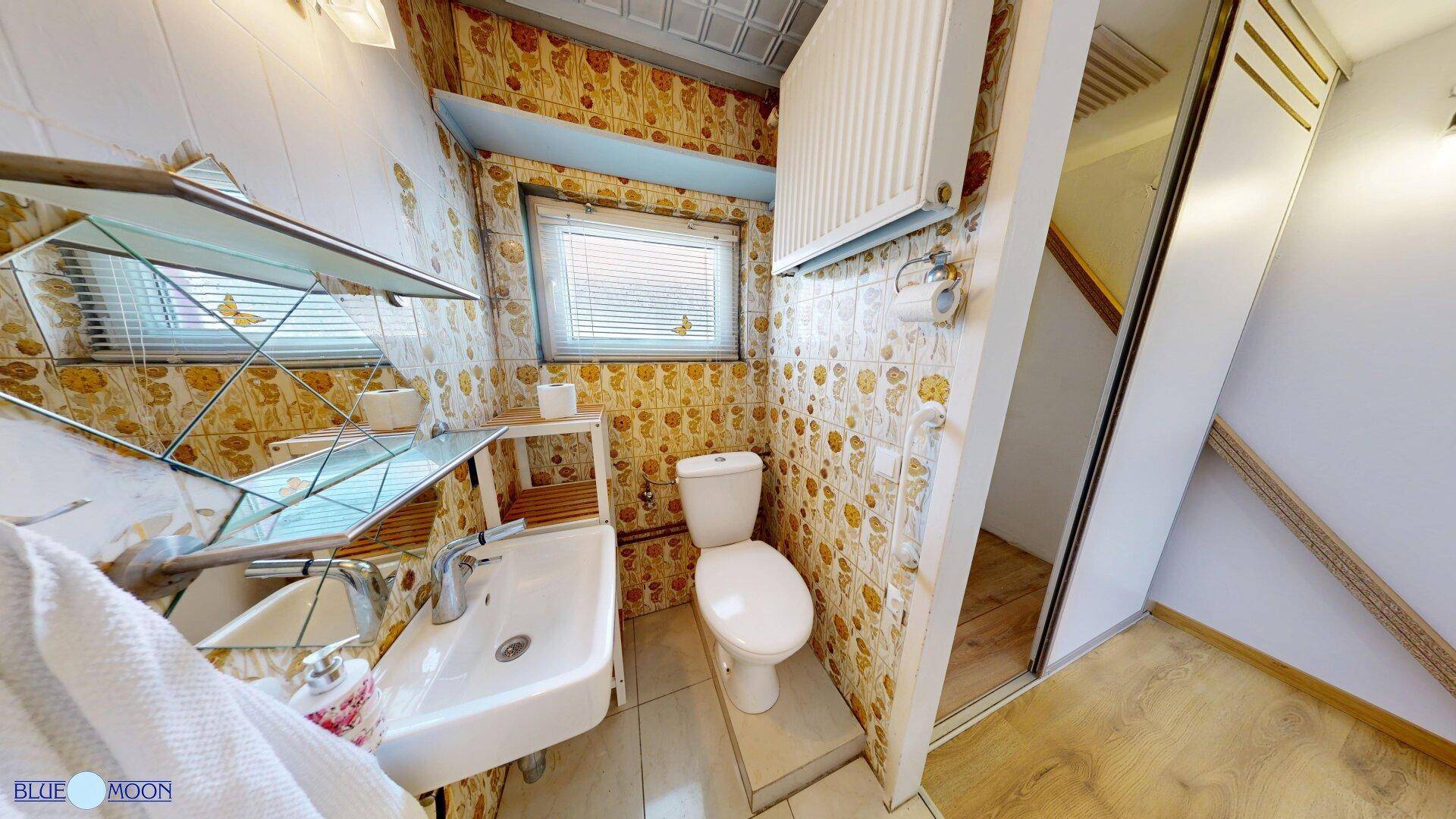 Kleines Badezimmer mit WC, Waschbecken und gemusterter Tapete.