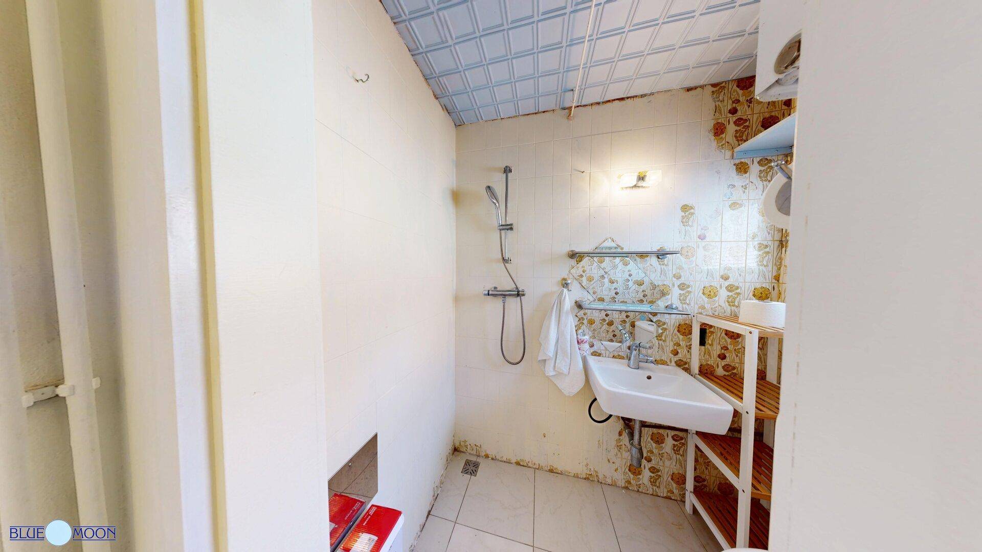 Duschbereich in einem kleinen Badezimmer mit Waschbecken und Fliesenboden.