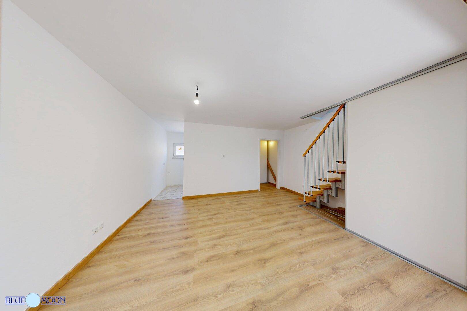 Geräumiger Wohnbereich mit Laminatboden und Blick auf die offene Treppe.