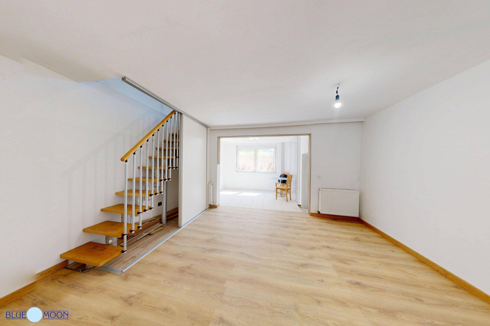 Heller Wohnbereich mit Laminatboden und offener Treppe, die in den oberen Bereich führt.