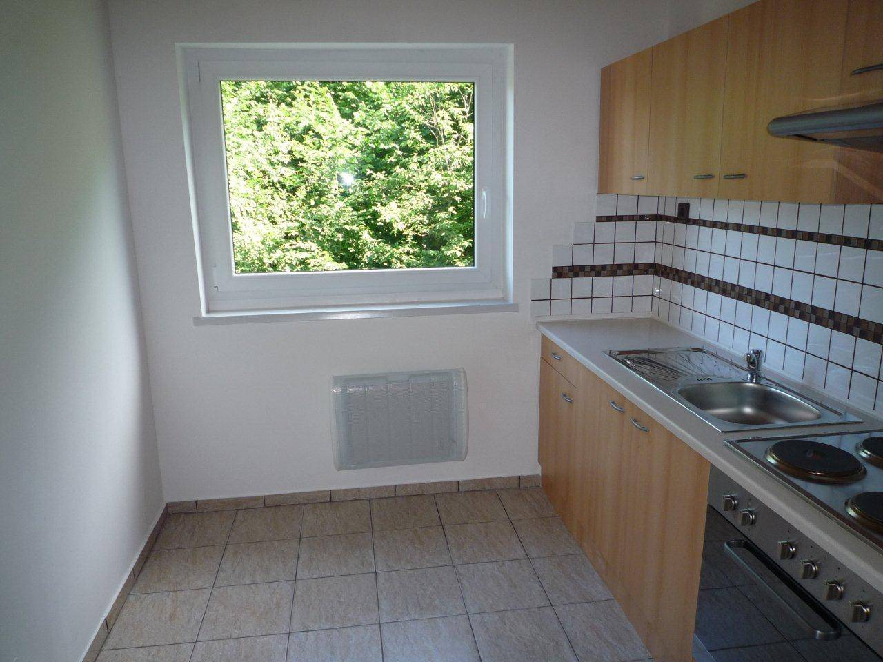 Funktionale Küche mit hellen Holzschränken, Fliesenboden und Fenster mit Blick ins Grüne.
