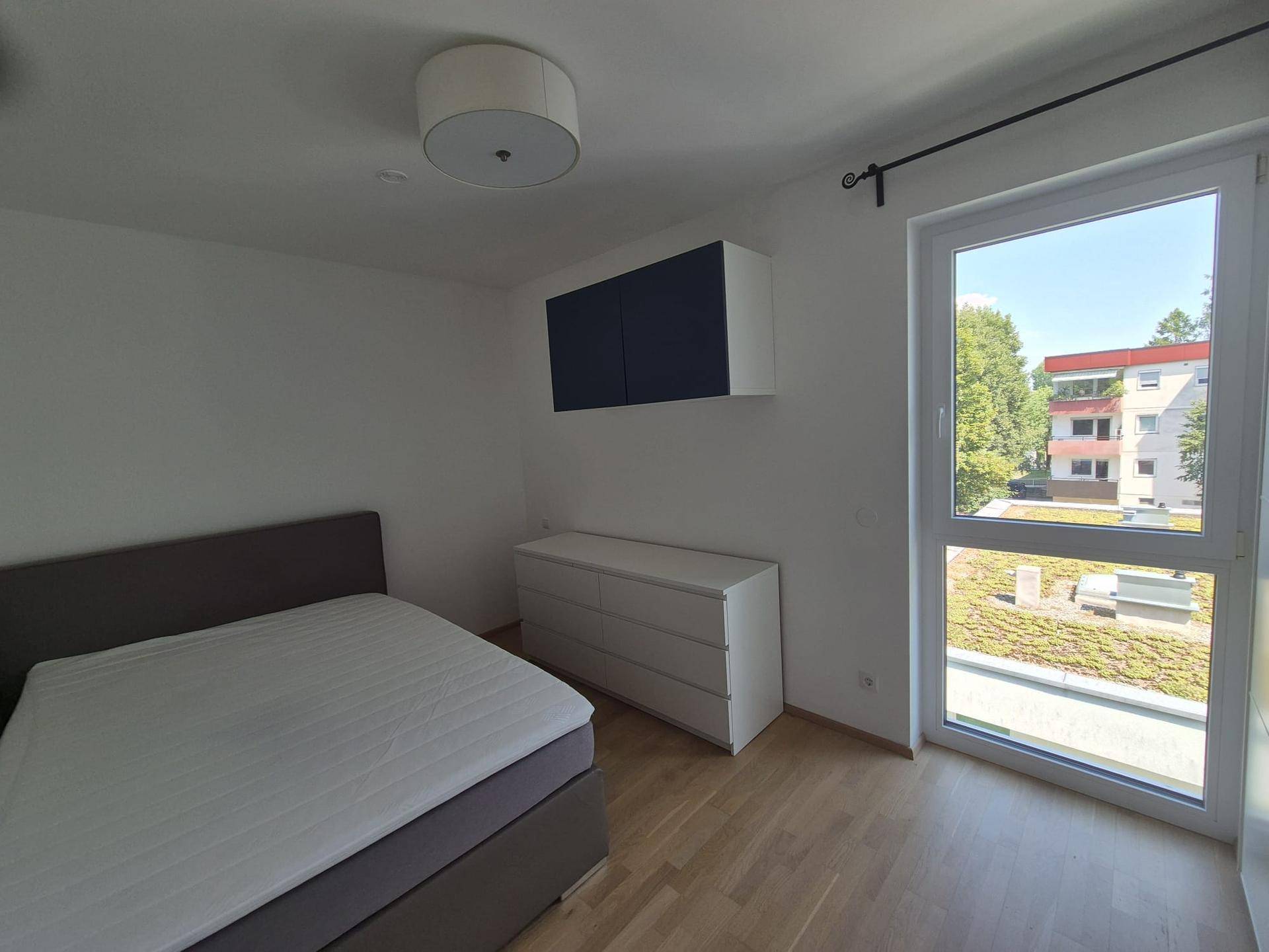Schlafzimmer mit Holzboden, großem Fenster und Blick ins Grüne.