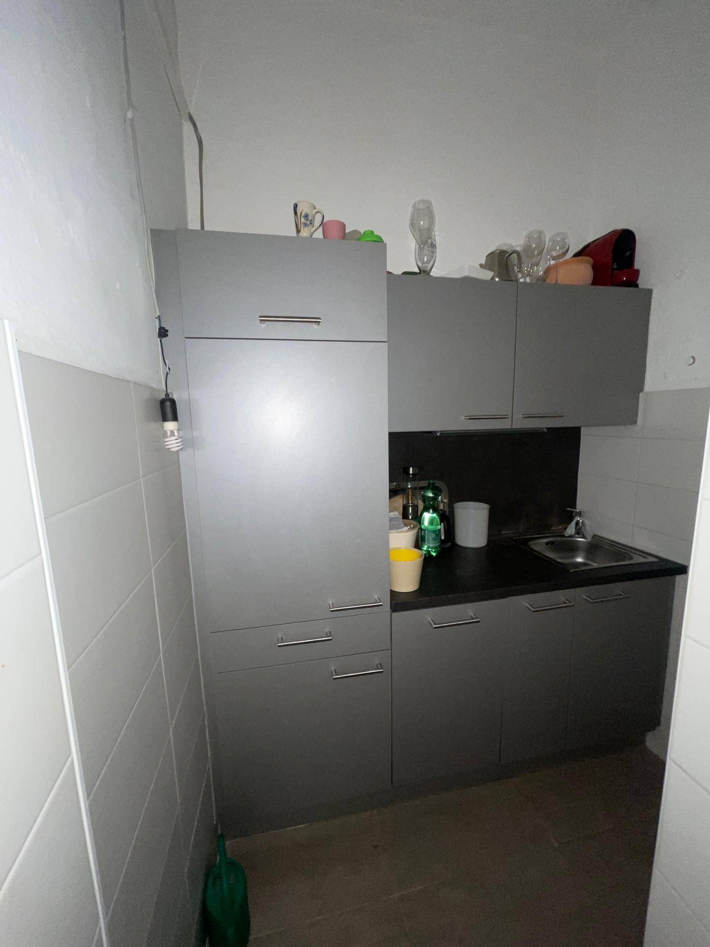 Kleine Küchenzeile mit grauen Schränken, Spüle und begrenztem Arbeitsbereich, funktional eingerichtet.