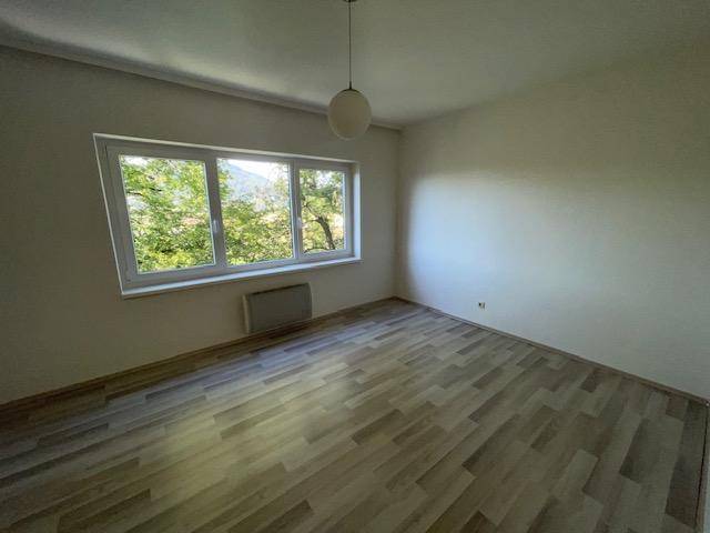Geräumiges Schlafzimmer mit hellem Laminatboden und einem großen Fenster mit Blick ins Grüne.