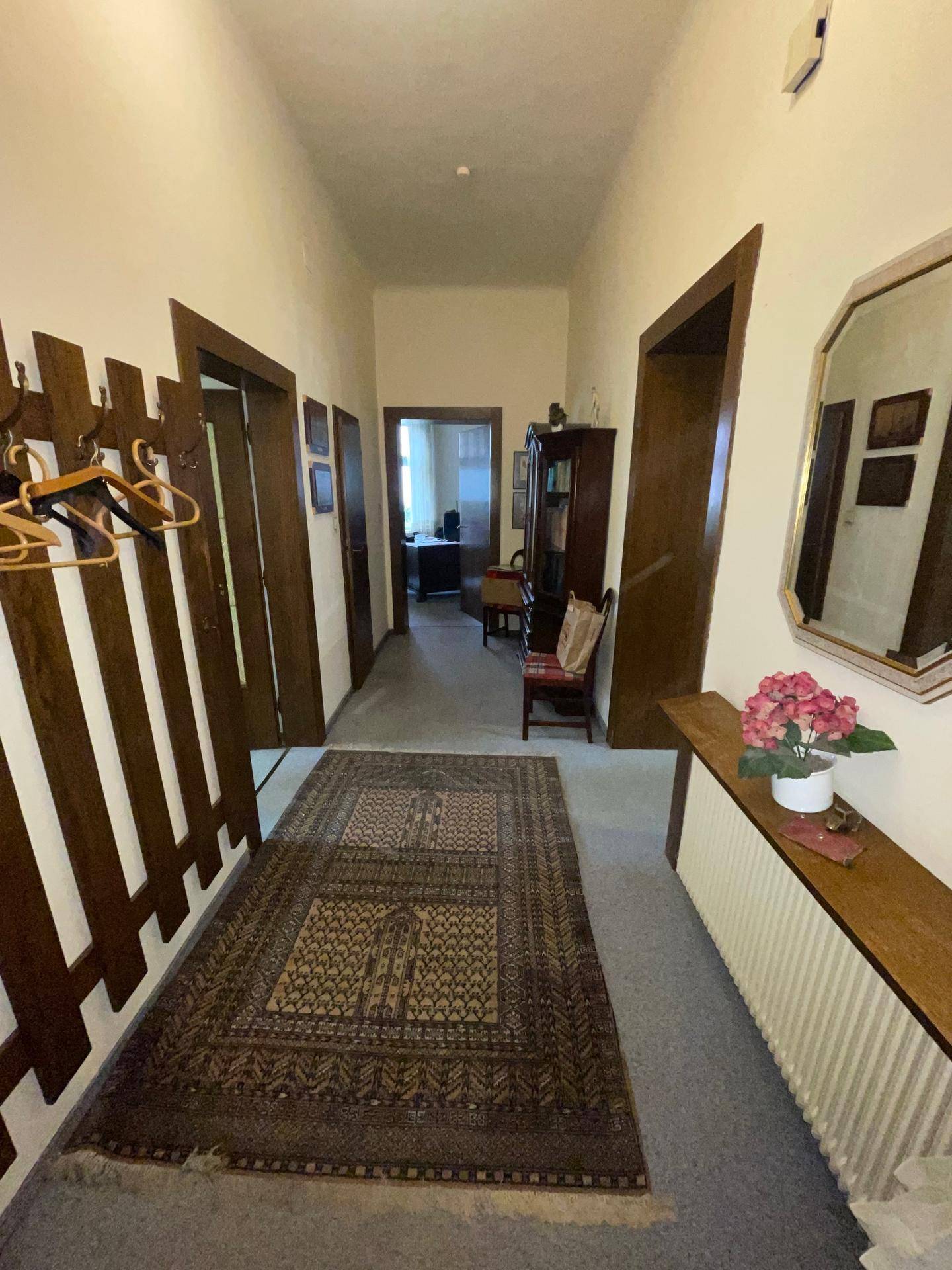 Heller Flur mit Teppich, Garderobe und Spiegel, der zu weiteren Räumen führt.