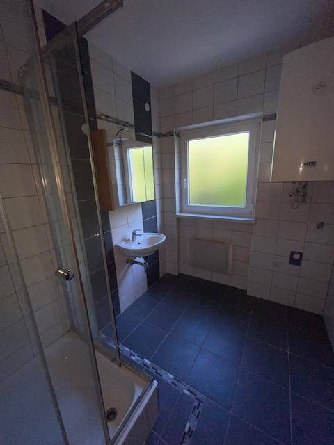 Modernes Badezimmer mit dunklen Bodenfliesen, Duschkabine, Waschbecken und Fenster für Tageslicht.