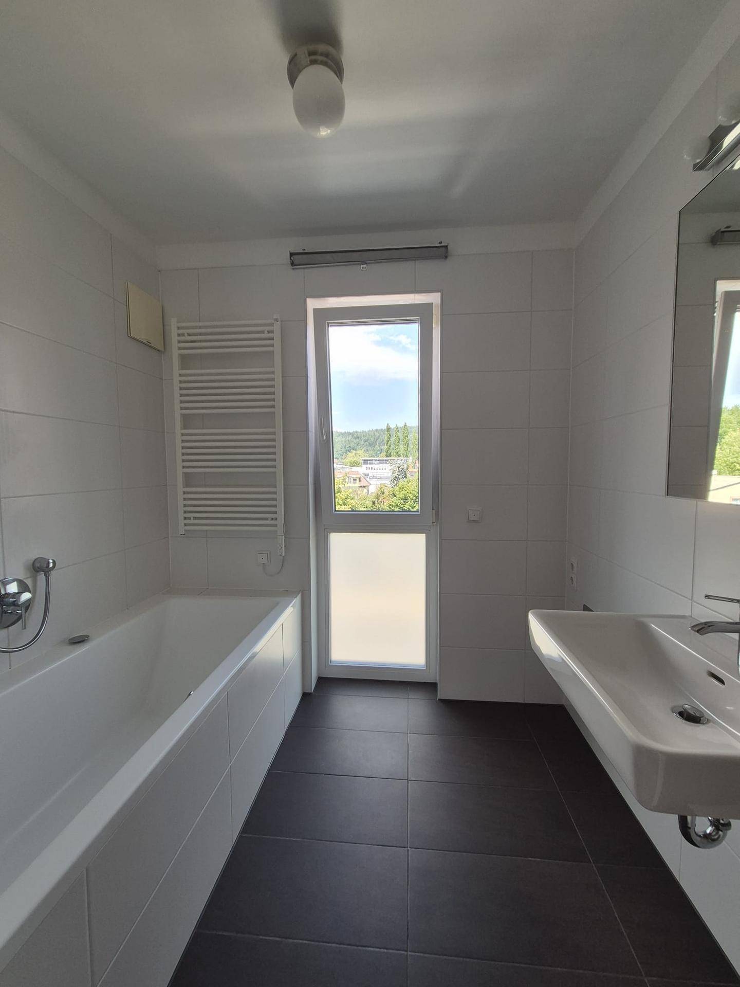Modernes Badezimmer mit Badewanne, Fenster und beheiztem Handtuchhalter.