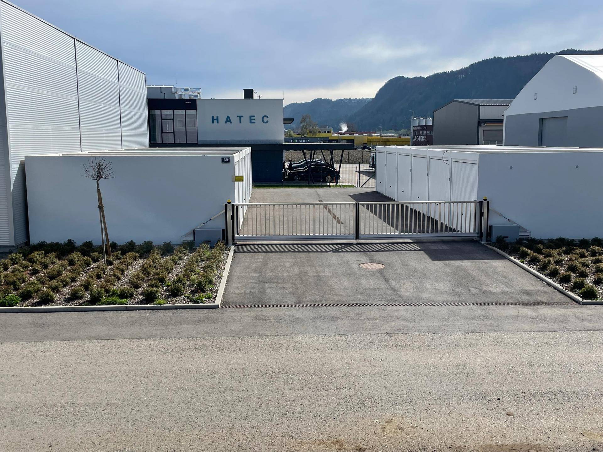Eingangsbereich eines modernen Gewerbekomplexes mit Schiebetor und Blick auf die umliegenden Berge.