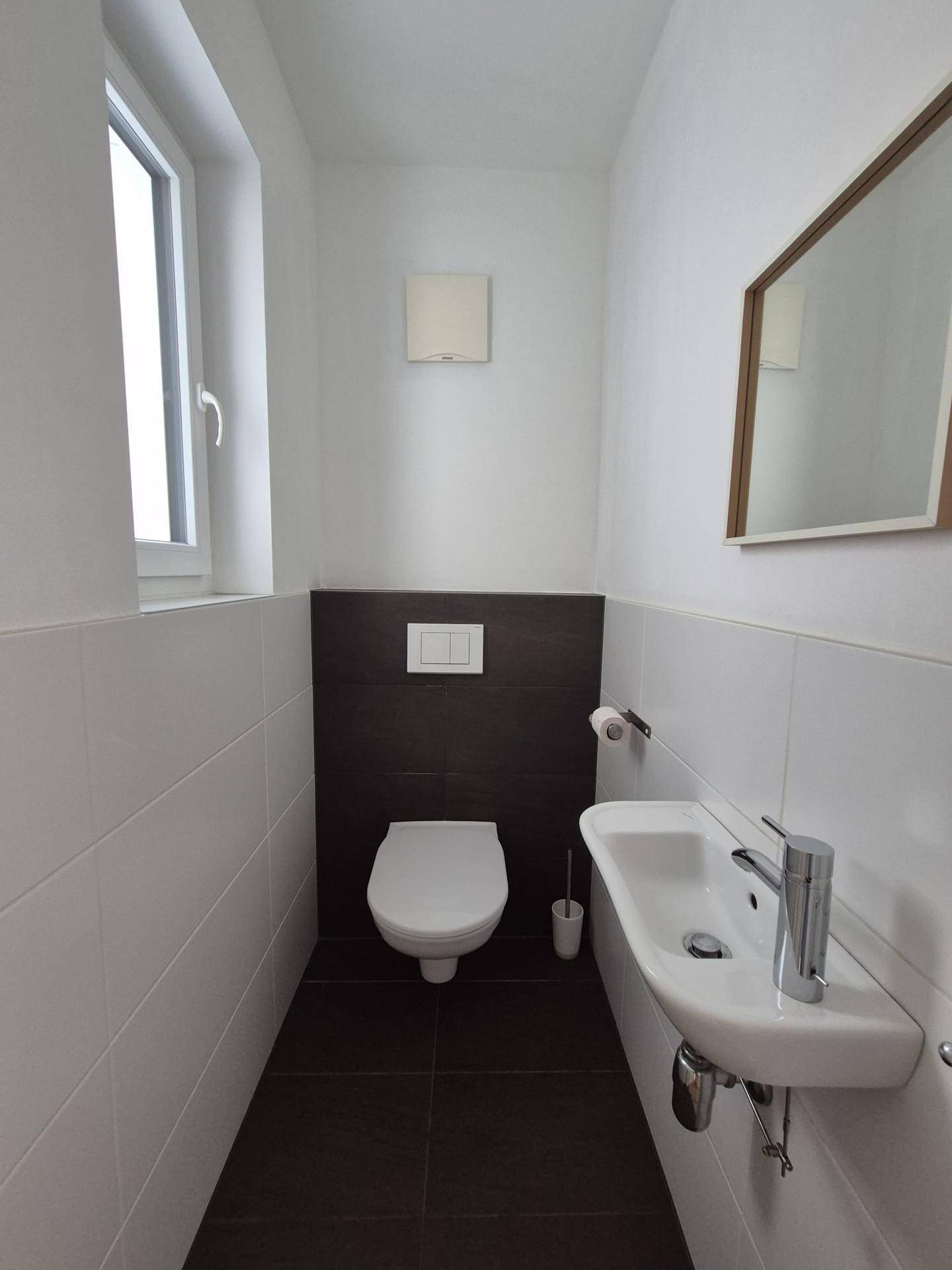 Separates Gäste-WC mit Fenster, Wand-WC und kleinem Waschbecken.