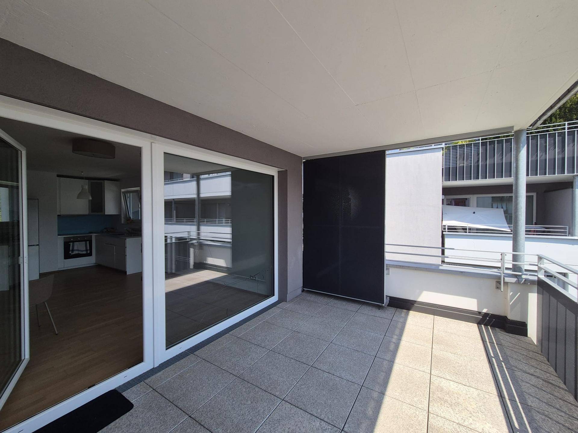 Heller Balkon mit Zugang zur Küche und Blick auf die moderne Wohnanlage.