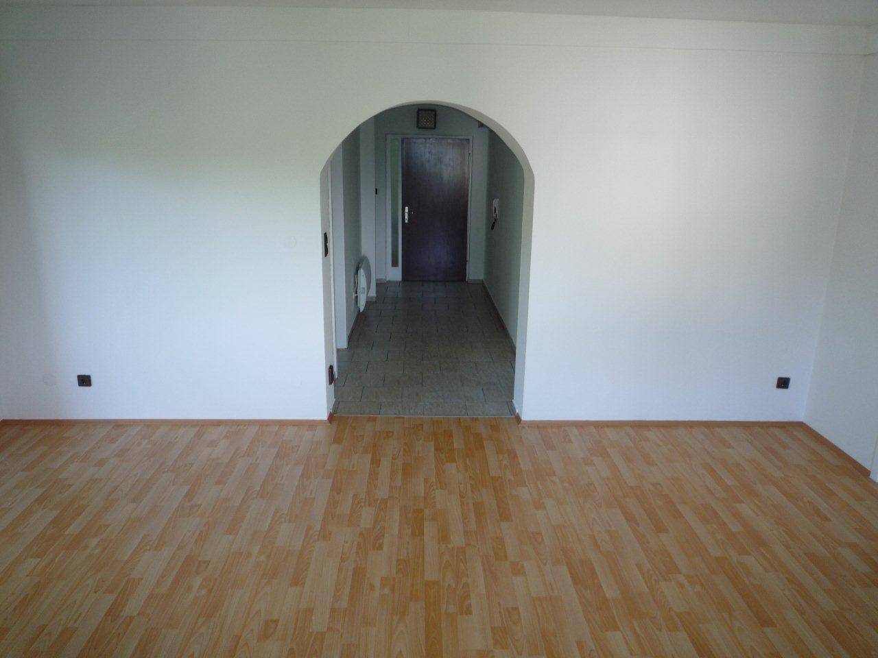 Wohnbereich mit Laminatboden und einem Rundbogen, der den Übergang zum Flur bildet.