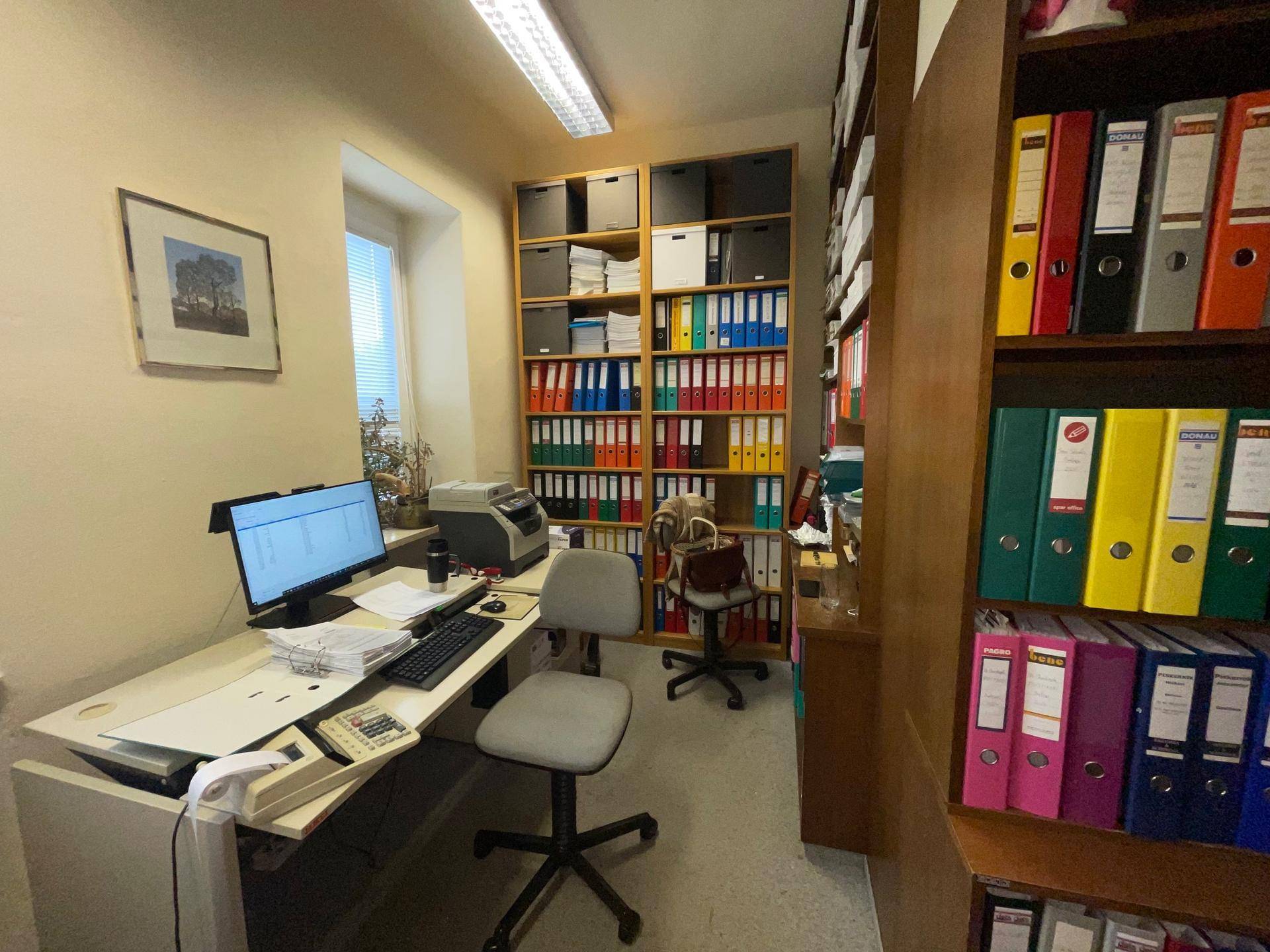 Kompaktes Büro mit Computerarbeitsplatz, Drucker und hohen Regalen voller Aktenordner.