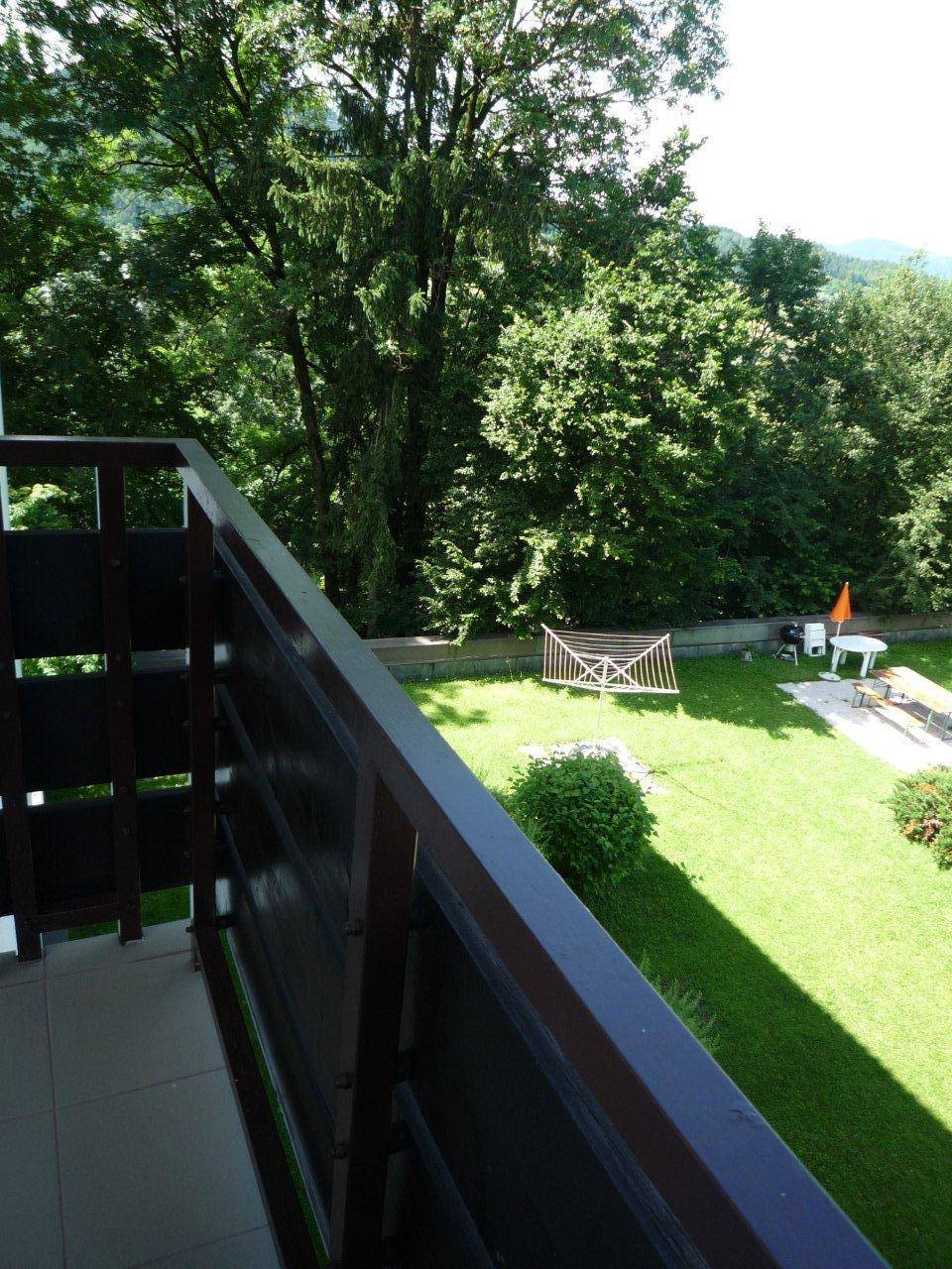 Blick vom Balkon auf einen gepflegten Gartenbereich mit Rasenfläche und Sitzgelegenheiten im Freien.