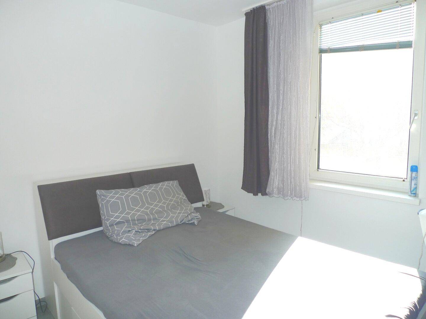 Schlafzimmer mit Doppelbett und großem Fenster, das viel Tageslicht hereinlässt.