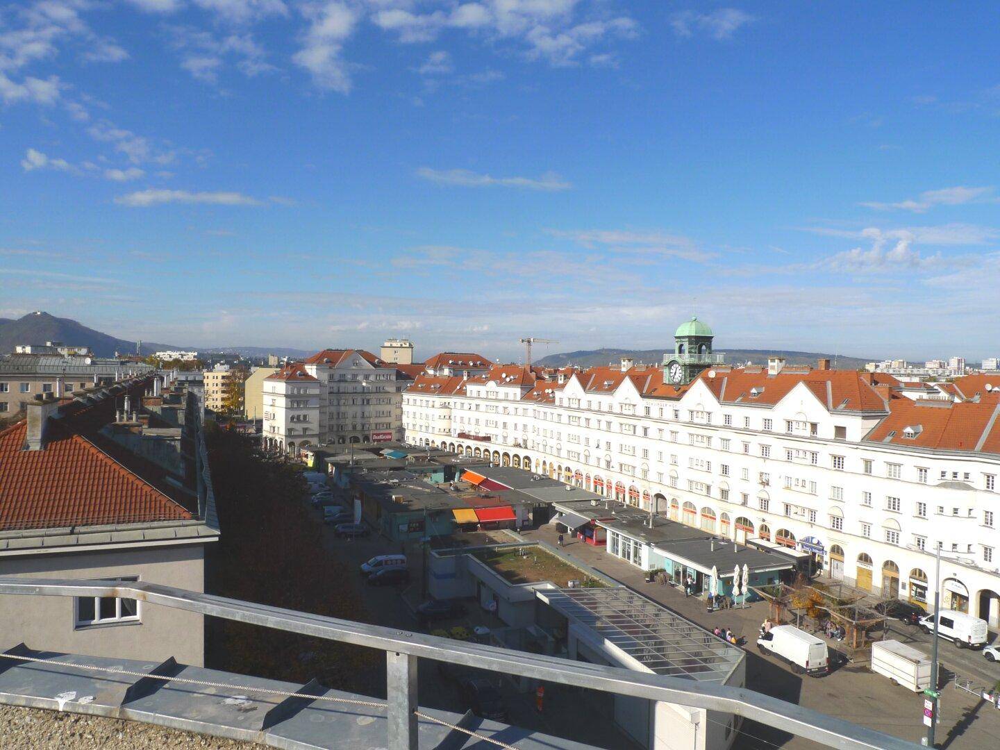 Weitläufiger Stadtblick über Dächer und Gebäude mit Bergen im Hintergrund.
