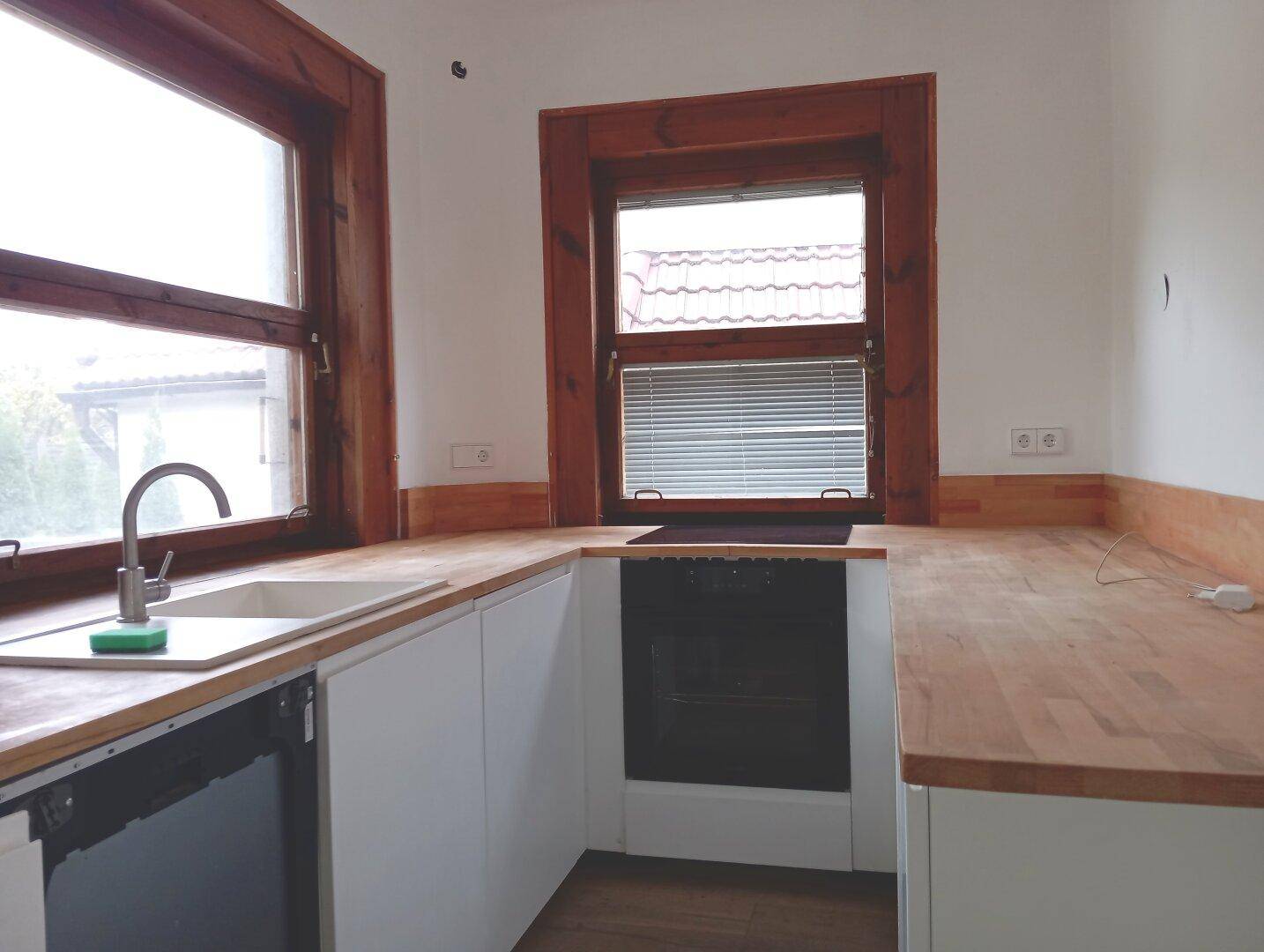 Funktionale Küche mit weißen Unterschränken, Holzarbeitsplatten und zwei Fenstern.