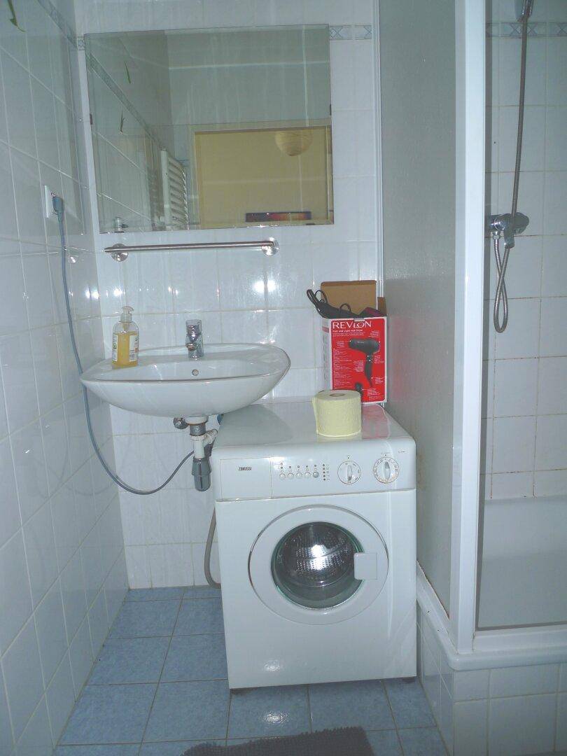 Funktionales Badezimmer mit Dusche, Waschbecken, Spiegel und einer integrierten Waschmaschine.