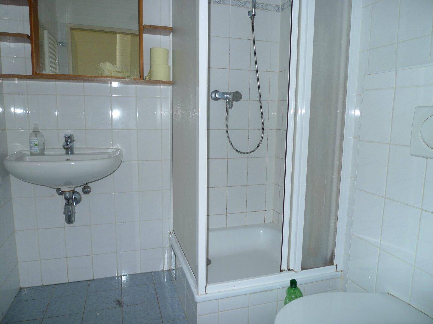 Kleines Badezimmer mit Dusche, Waschbecken und weißen Fliesen.