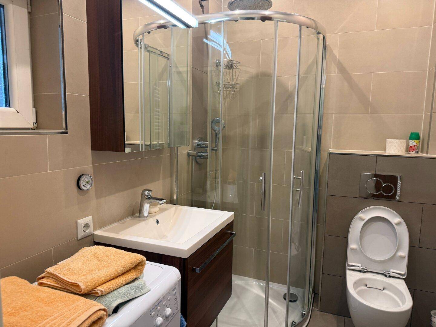 Modernes Badezimmer mit Eckdusche, Waschbecken und integrierter Waschmaschine.
