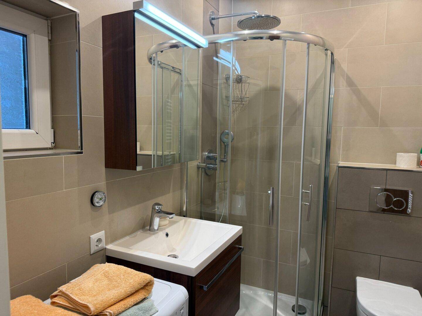 Helles Badezimmer mit Fenster, Duschkabine und modernem Waschtisch.