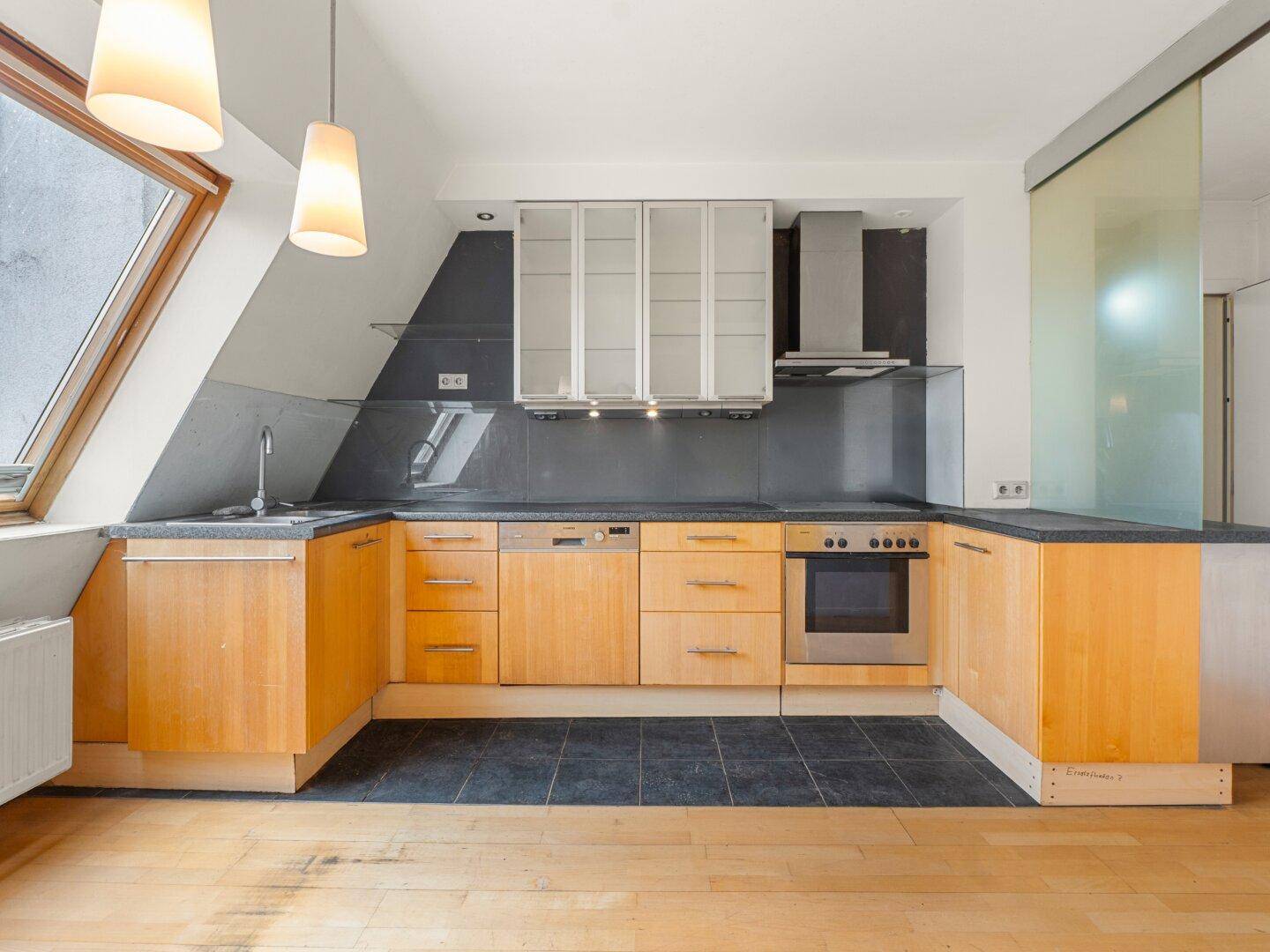 Funktionale Küche mit Holzschränken, dunklen Arbeitsplatten und integrierten Geräten unter Dachschräge.