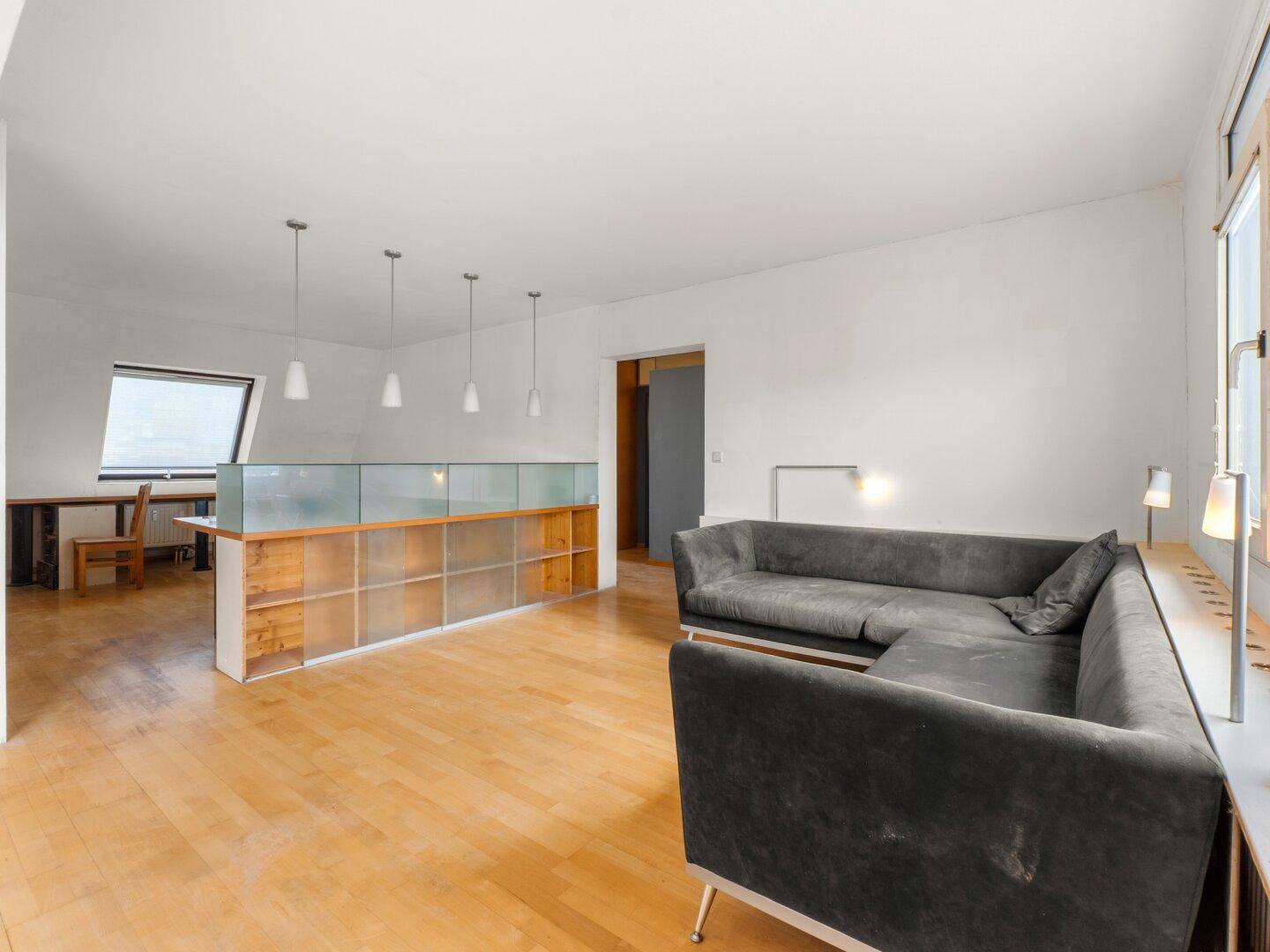 Gemütliches Wohnzimmer mit L-förmigem Sofa, Holzfußboden und einer stilvollen Raumtrennung.