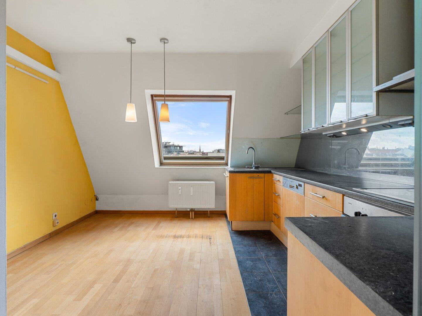 Offene Küche mit gelber Akzentwand, Holzfußboden und einem großen Dachfenster.